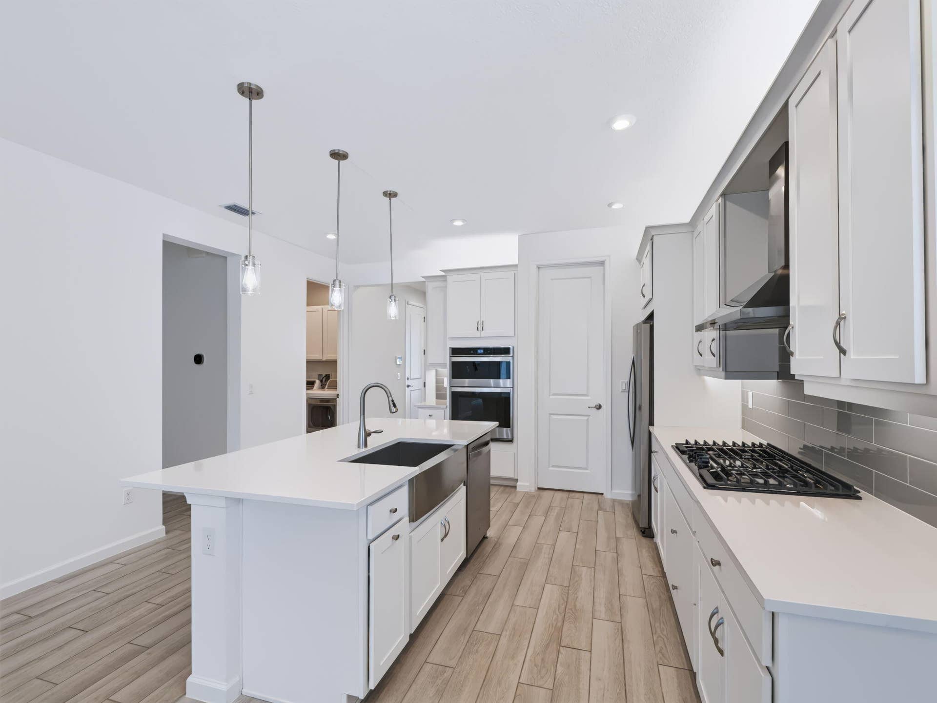 12688 SW Eleanor Drive, Port St Lucie, FL 34987 Kitchen featuring white cabinetry, an expansive island with a stainless steel farmhouse sink, gas cooktop, built-in double wall ovens, and wood-finish flooring