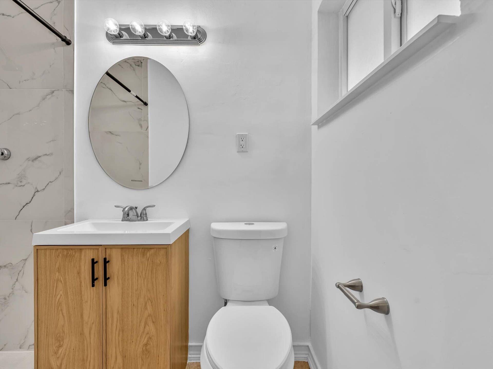 132 SE 2ND Court, Dania Beach, Dania Beach, FL 33004 Bathroom featuring a wood-finish vanity, oval wall-mounted mirror, light-toned stone-style tile shower surround, and a four-light chrome vanity fixture