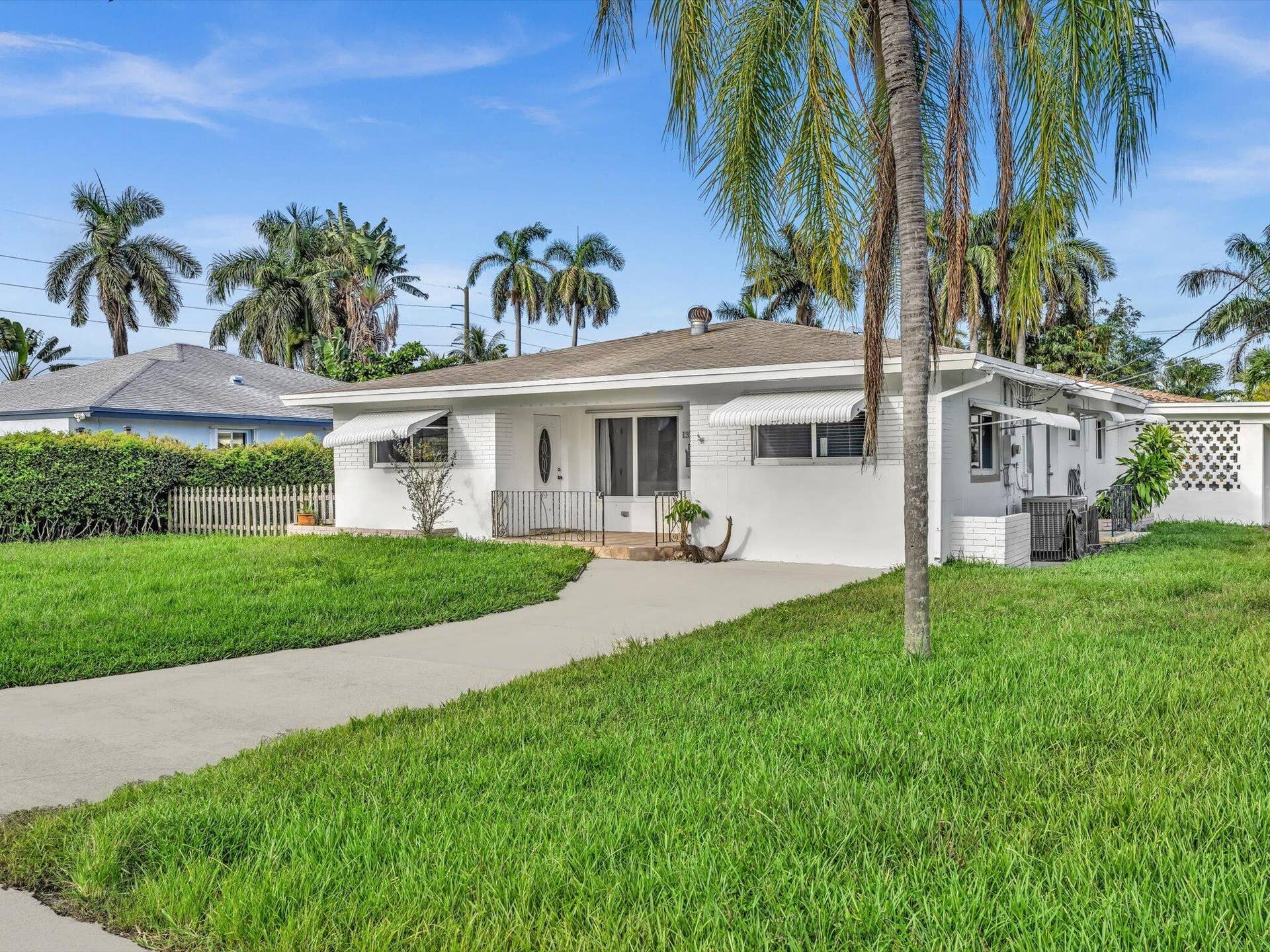 132 SE 2ND Court, Dania Beach, Dania Beach, FL 33004 White painted brick exterior featuring a concrete driveway, metal window awnings, and an arched entryway with iron railing