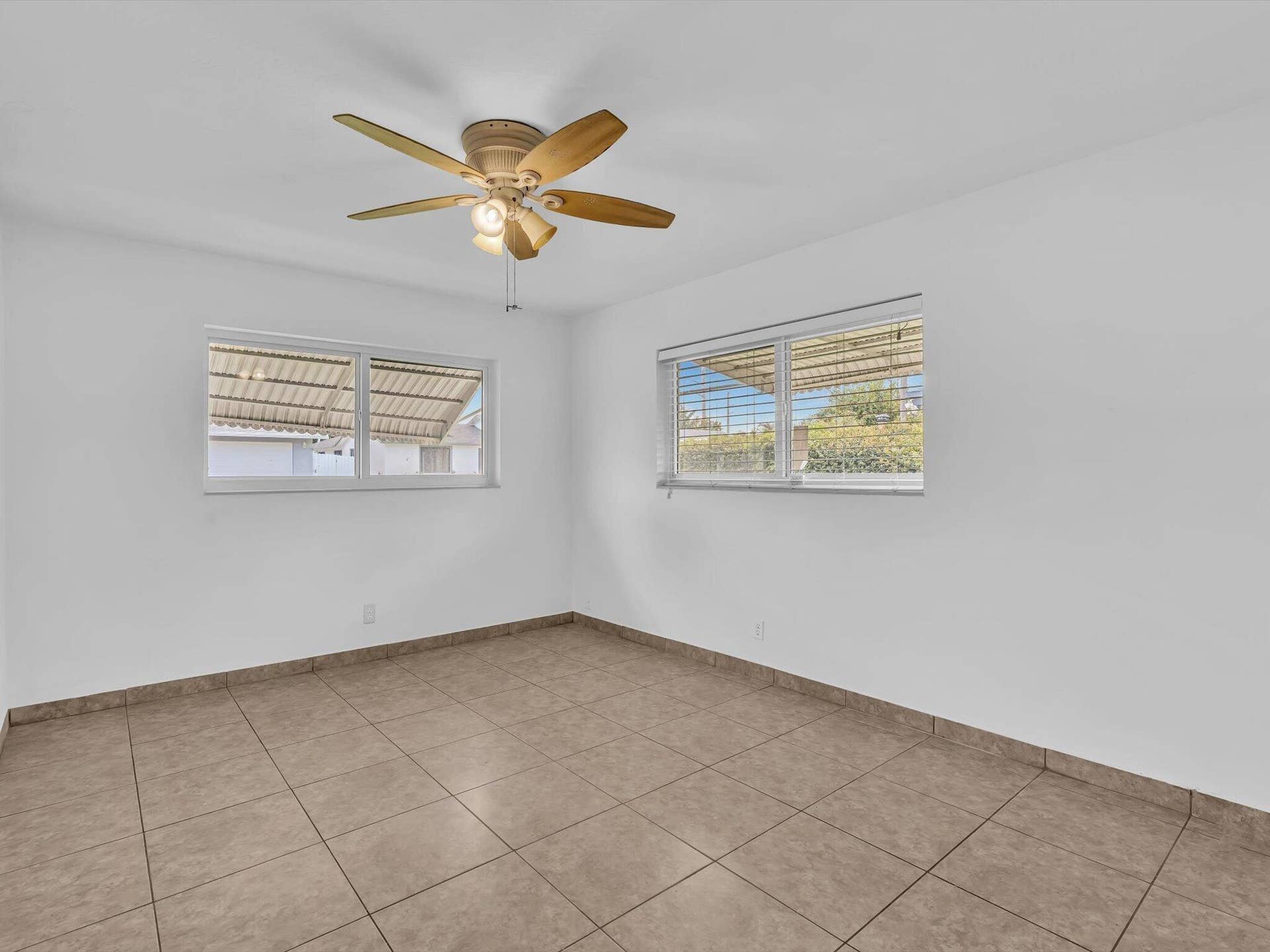 132 SE 2ND Court, Dania Beach, Dania Beach, FL 33004 Neutral interior space featuring large-format tile flooring, dual windows with exterior metal awnings, and a five-blade ceiling fan with integrated lighting