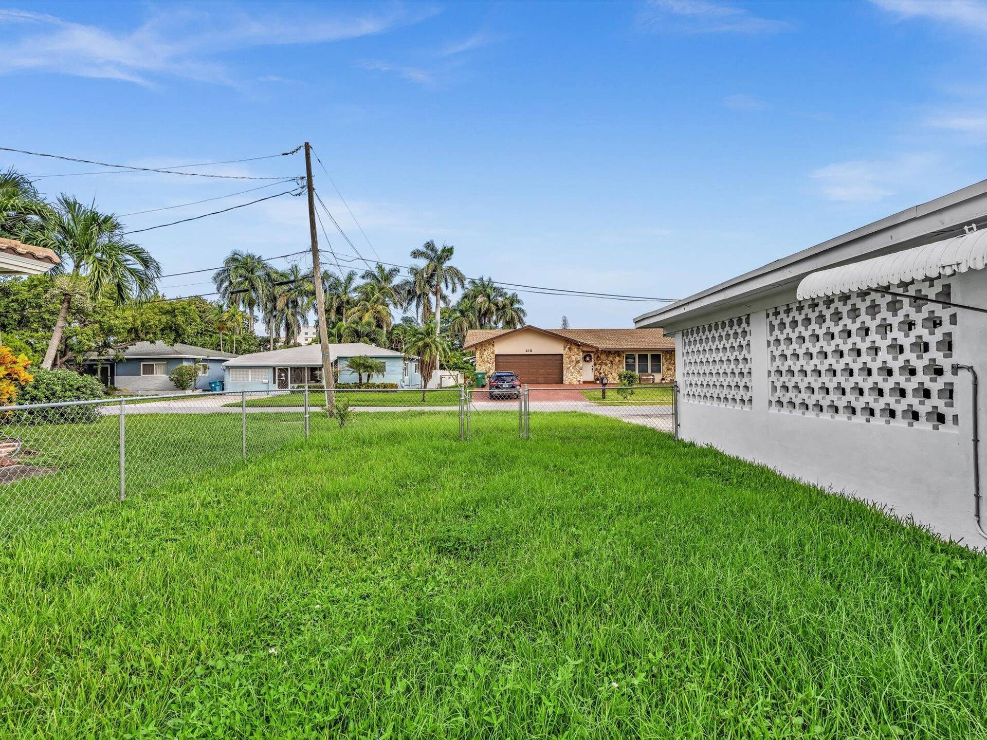132 SE 2ND Court, Dania Beach, Dania Beach, FL 33004 Exterior of property featuring a lawn, chain-link fencing, and white masonry screen wall with an attached metal awning