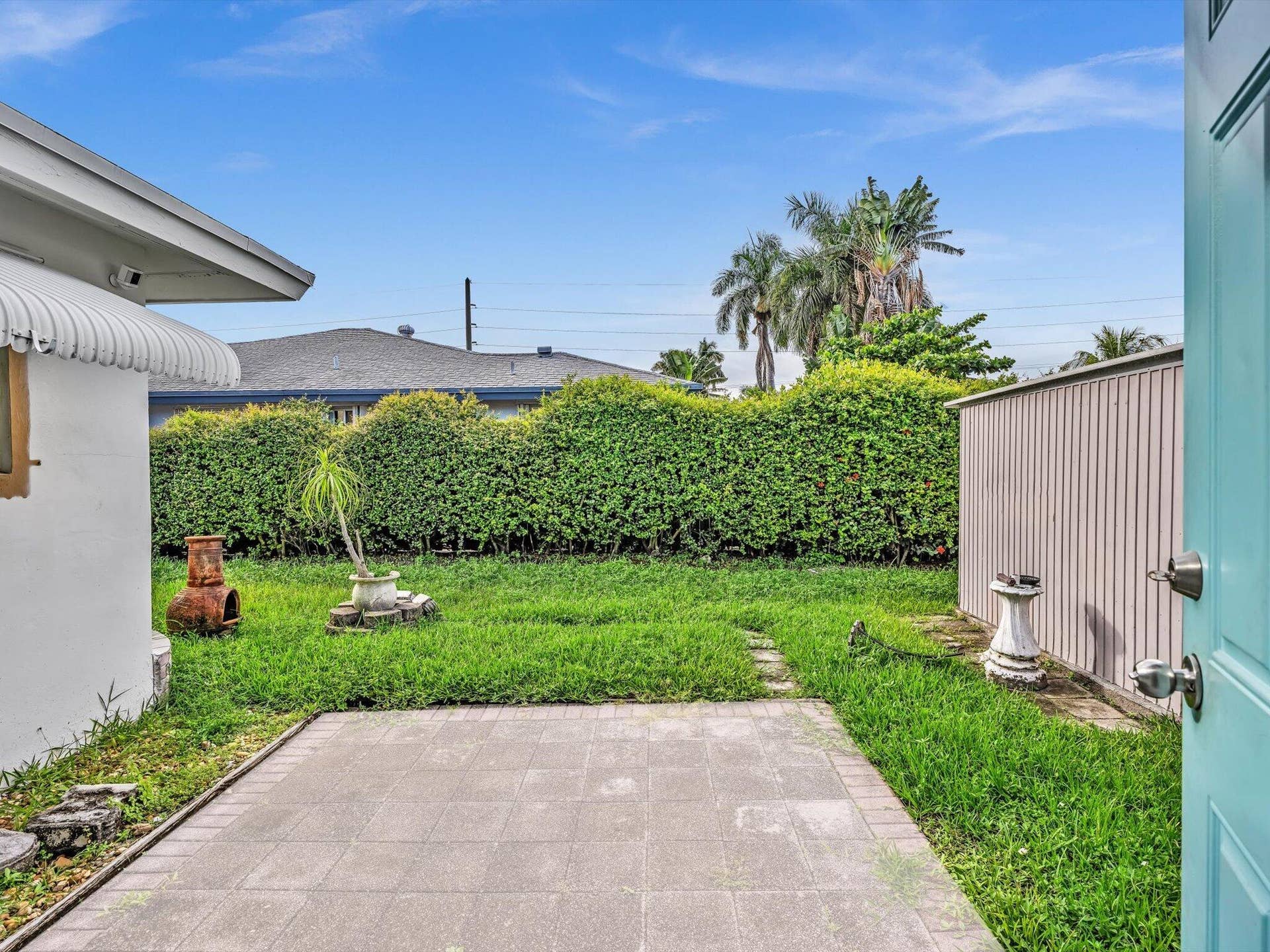 132 SE 2ND Court, Dania Beach, Dania Beach, FL 33004 Rear exterior space featuring a paved stone patio, manicured lawn, established privacy hedges, and an external metal storage structure