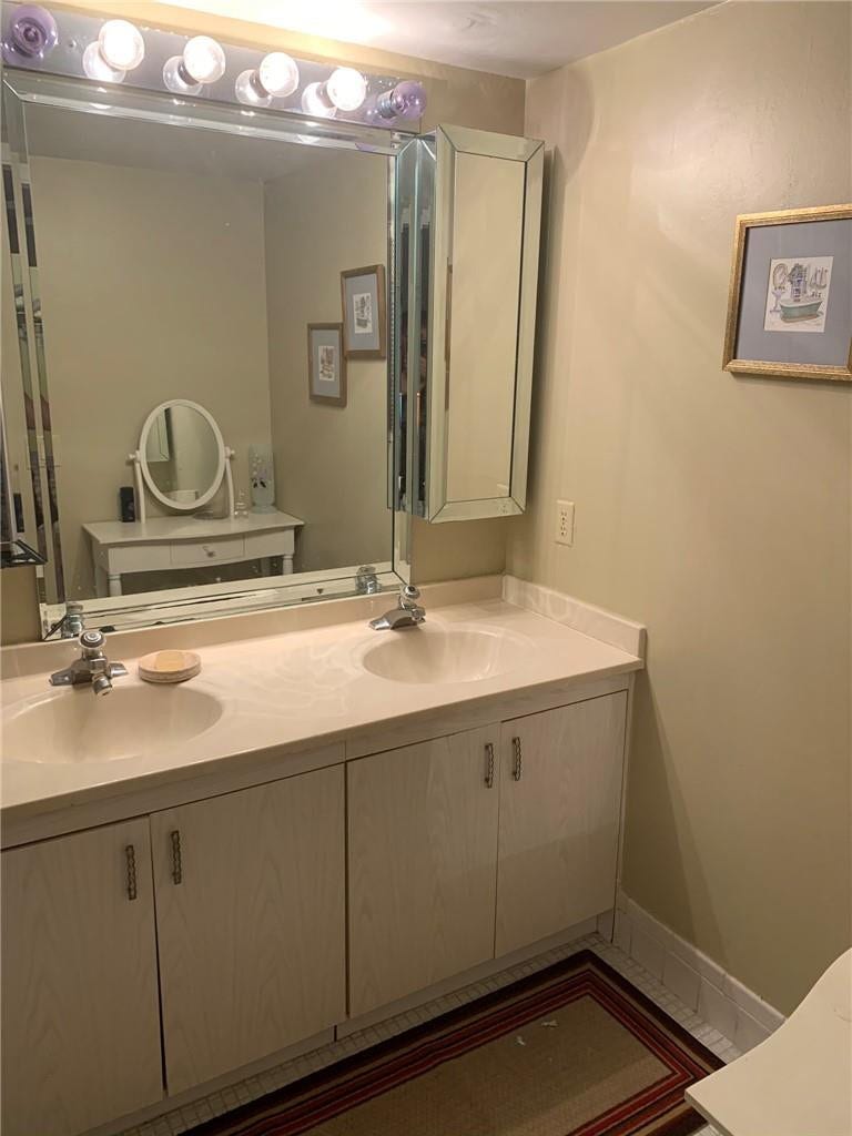 2305 LUCAYA Lane, #L4, Coconut Creek, Coconut Creek, FL 33066 Dual-sink vanity with a solid-surface countertop, integrated mirrored medicine cabinet, full-width wall mirror, and multi-bulb Hollywood-style light fixture