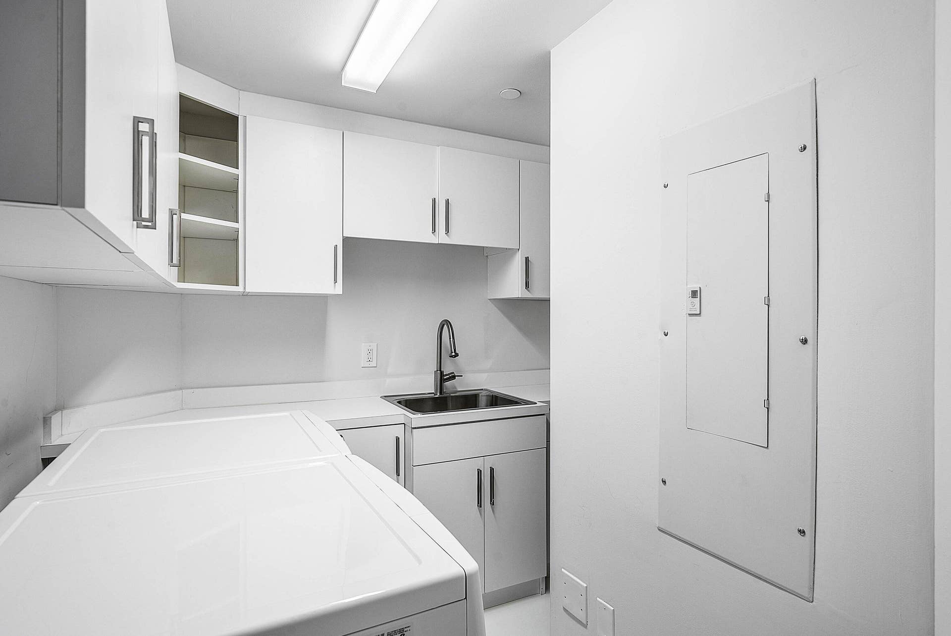 Laundry area featuring white cabinetry, integrated open shelving, a stainless steel sink with a high-arc faucet, and solid-surface countertops