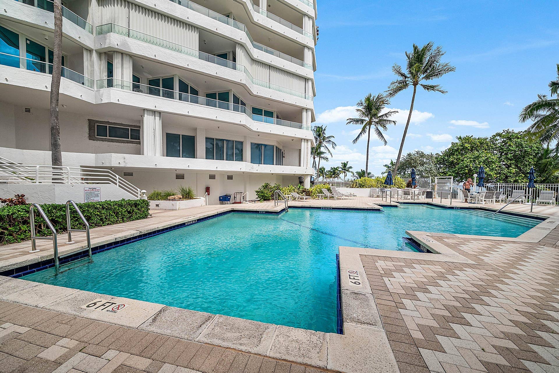 Swimming pool with paver decking, metal handrails, and surrounding mature palm trees