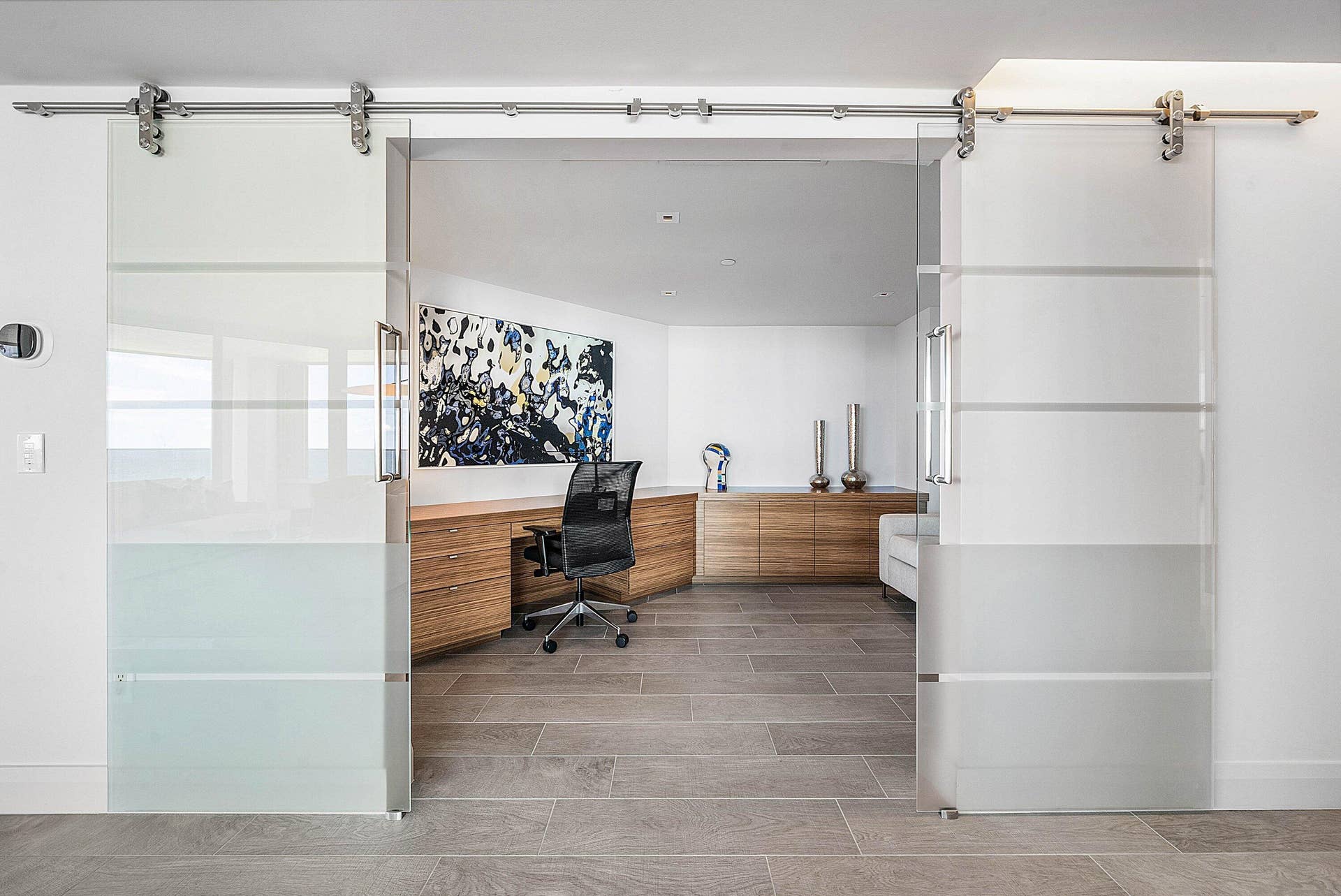 Dual frosted glass sliding doors with stainless steel hardware, wood-finish built-in cabinetry, recessed lighting, and large-format tile flooring