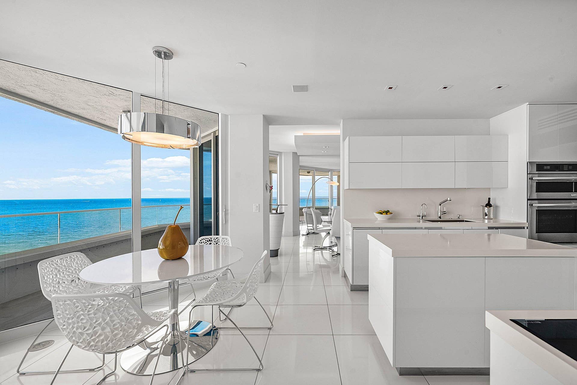 Floor-to-ceiling glass paneling, high-gloss white cabinetry, center island with stone countertop, large-format tile flooring, and integrated stainless steel double wall ovens