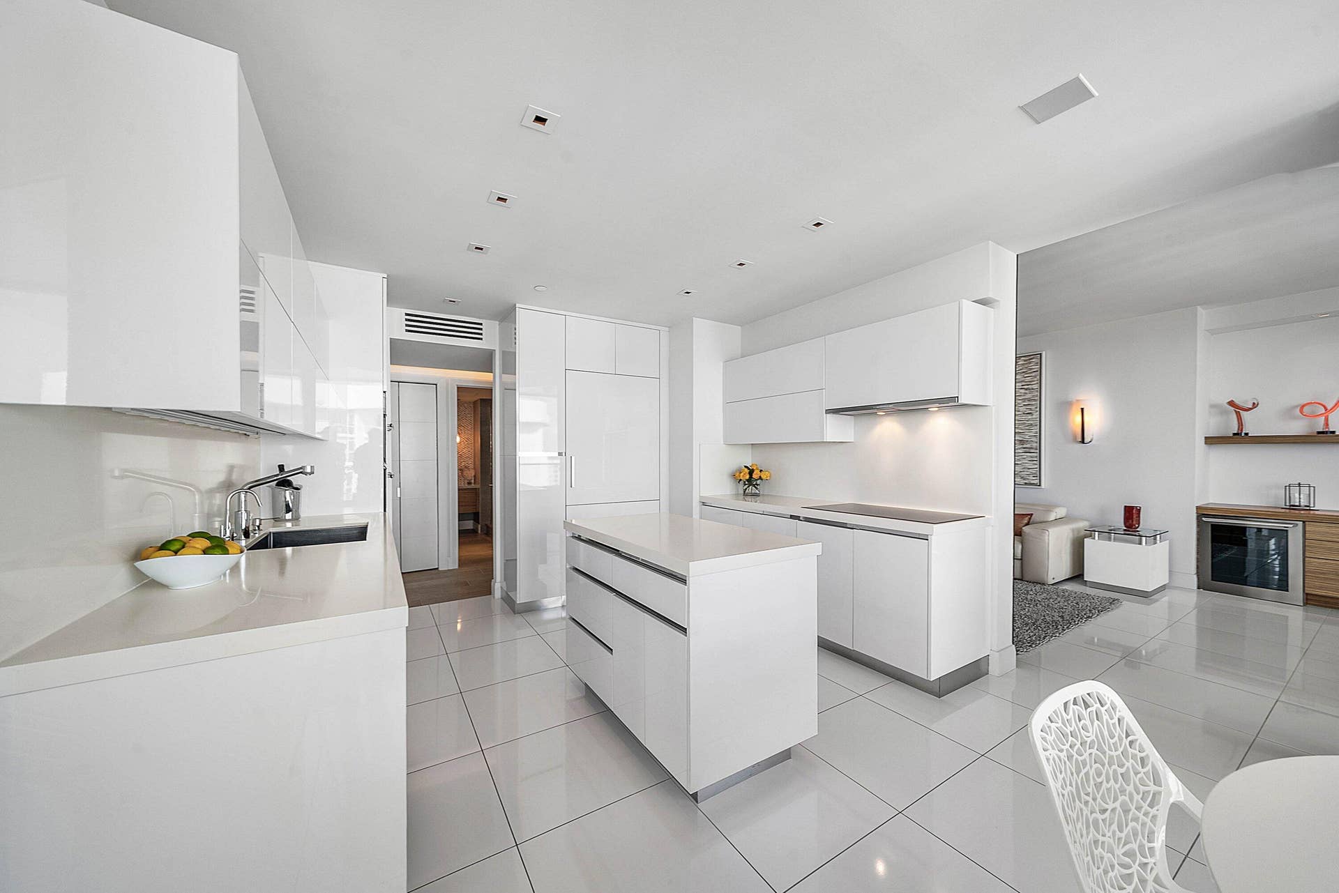 Minimalist kitchen featuring high-gloss white cabinetry, quartz countertops, a central island, recessed ceiling lighting, and polished tile flooring