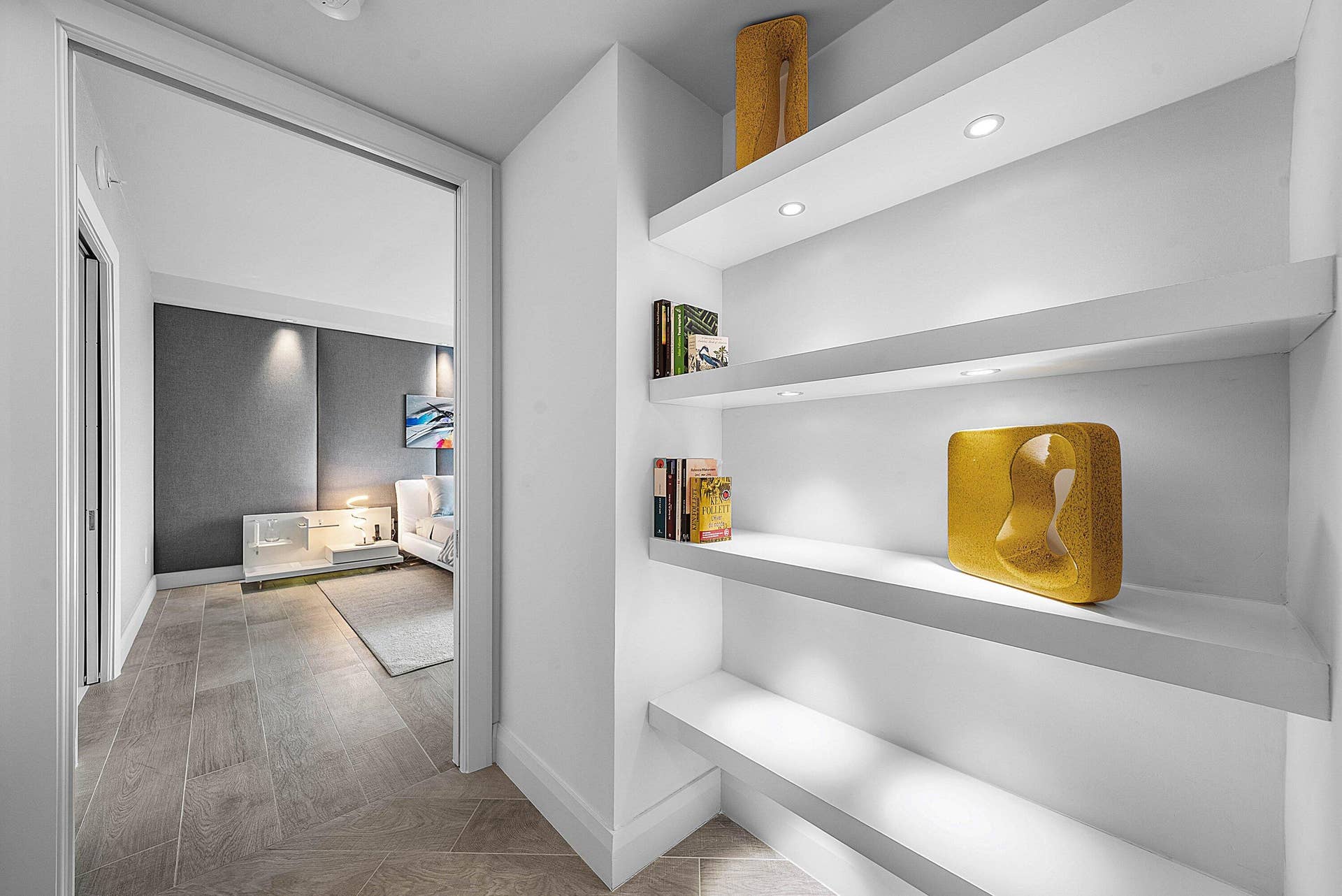 Built-in white floating shelving with integrated recessed lighting and wood-finish tile flooring