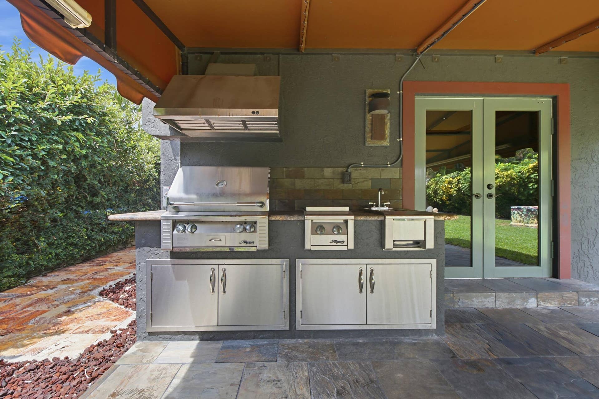 1110 SW 18TH Court, Fort Lauderdale, FL 33315 Outdoor kitchen featuring stainless steel built-in grill, dual-burner cooktop, integrated sink, stone countertop, and stainless steel cabinetry under a covered patio