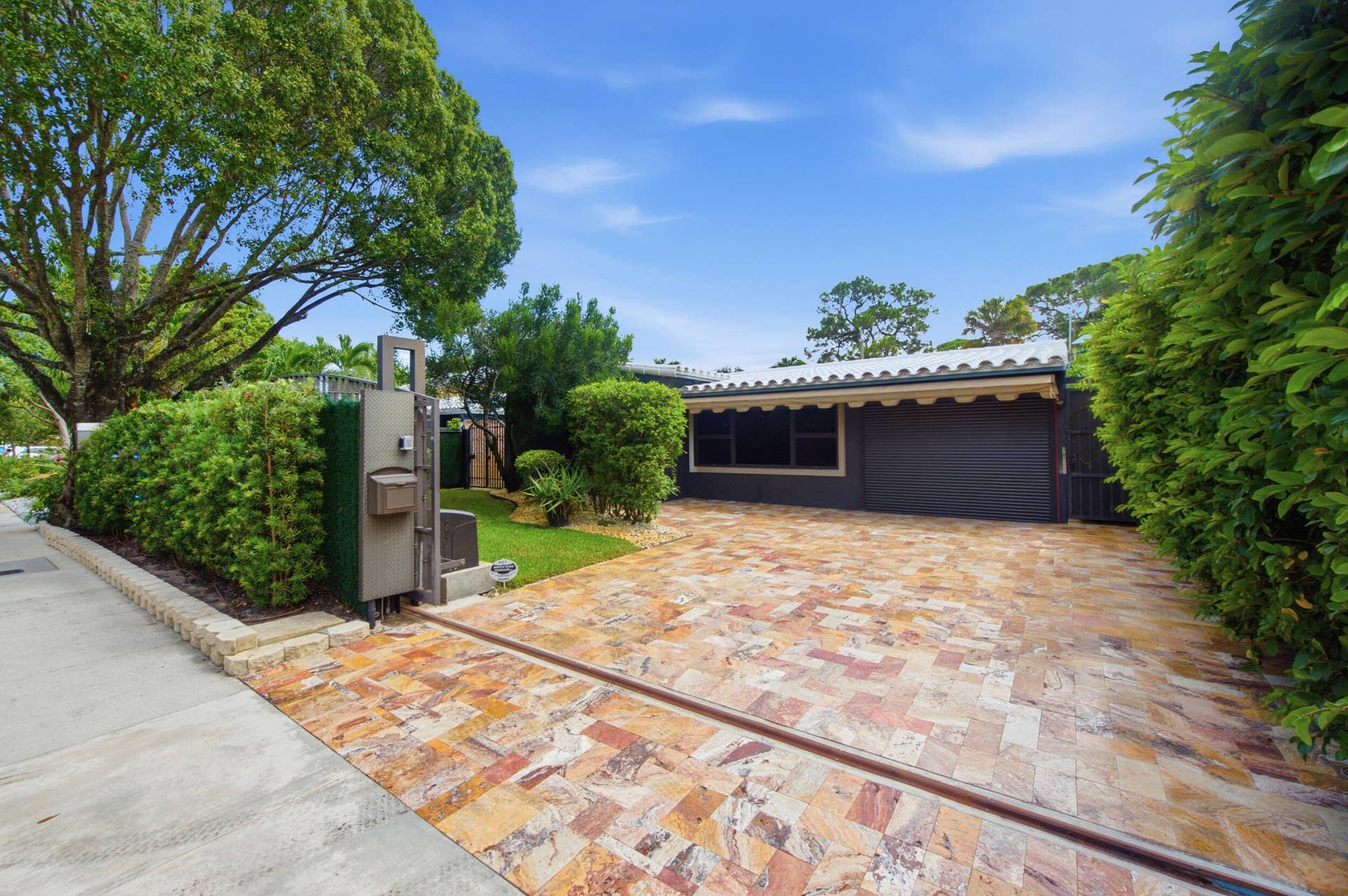 1110 SW 18TH Court, Fort Lauderdale, FL 33315 Herringbone-patterned stone driveway, gated entry, mature privacy hedging, tile roof, and enclosed garage