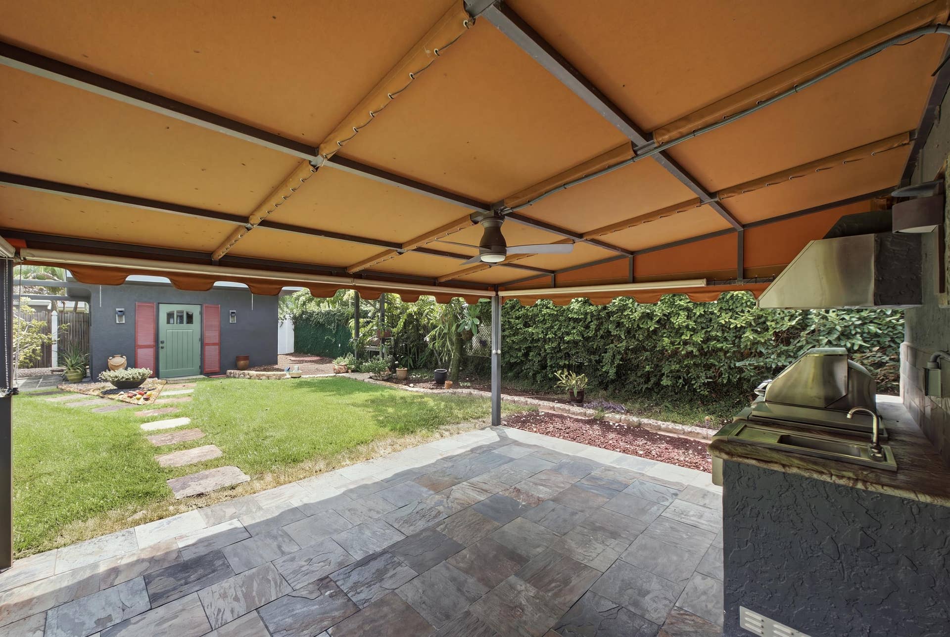 1110 SW 18TH Court, Fort Lauderdale, FL 33315 Covered outdoor patio featuring stone tile flooring, a built-in outdoor kitchen with stainless steel grill and sink, and a ceiling fan