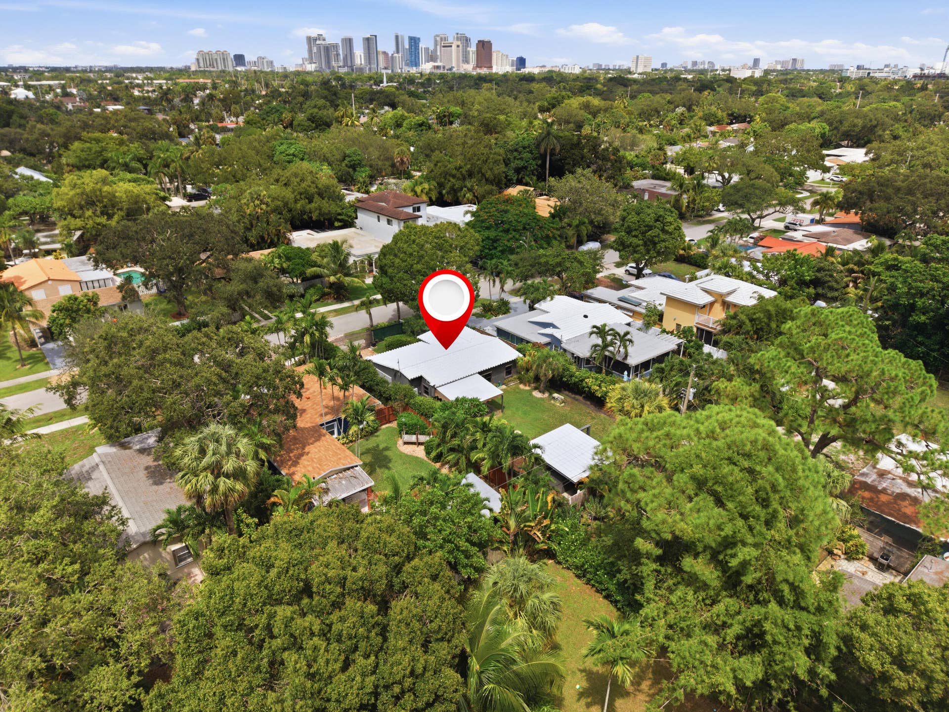 1110 SW 18TH Court, Fort Lauderdale, FL 33315 Aerial perspective of the residential lot featuring a metal roof structure, mature landscaping, and a defined backyard area, set against a distant skyline