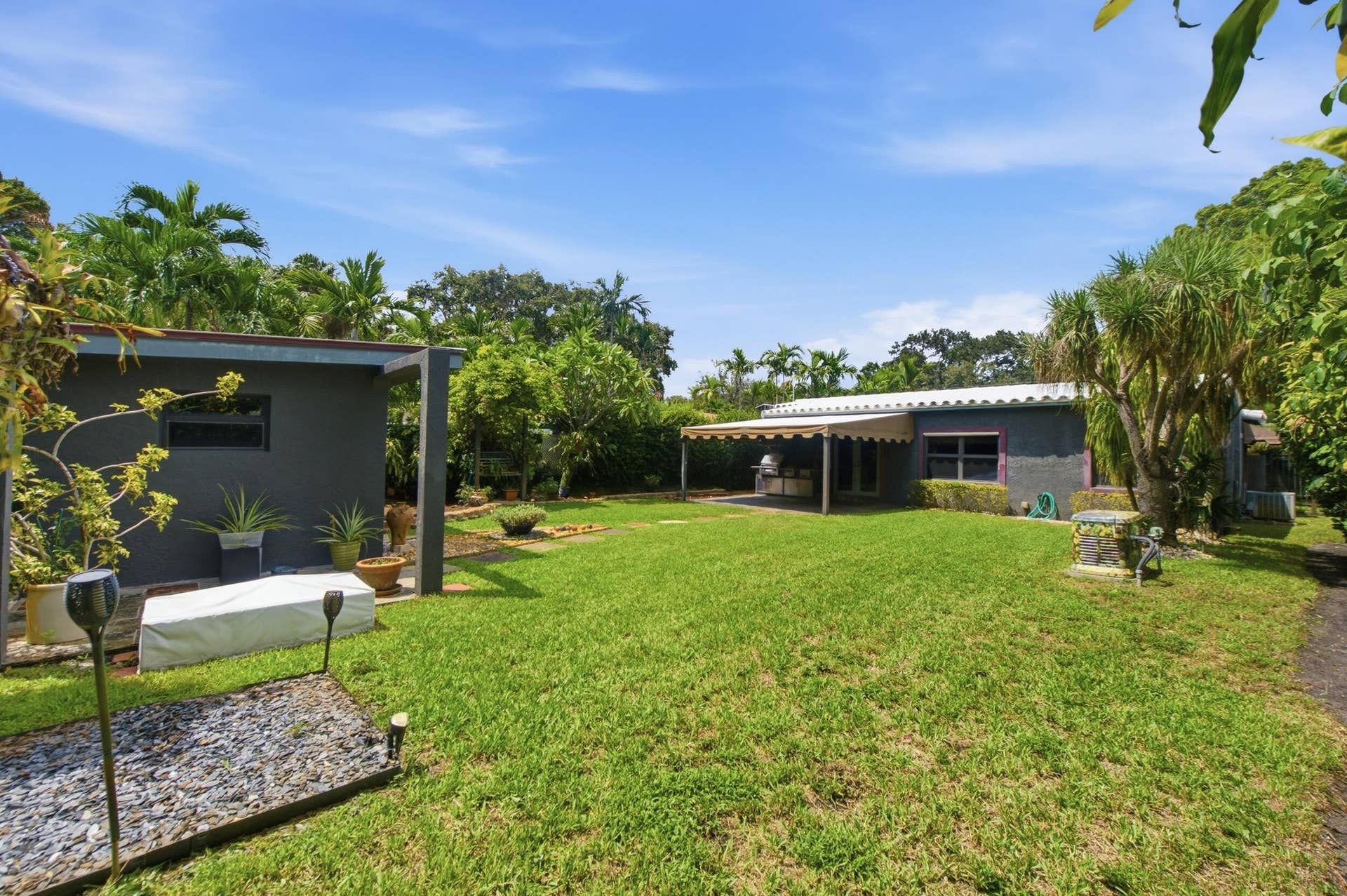 1110 SW 18TH Court, Fort Lauderdale, FL 33315 Expansive backyard featuring a manicured lawn, detached structure, covered patio, mature landscaping, and hardscaped garden beds
