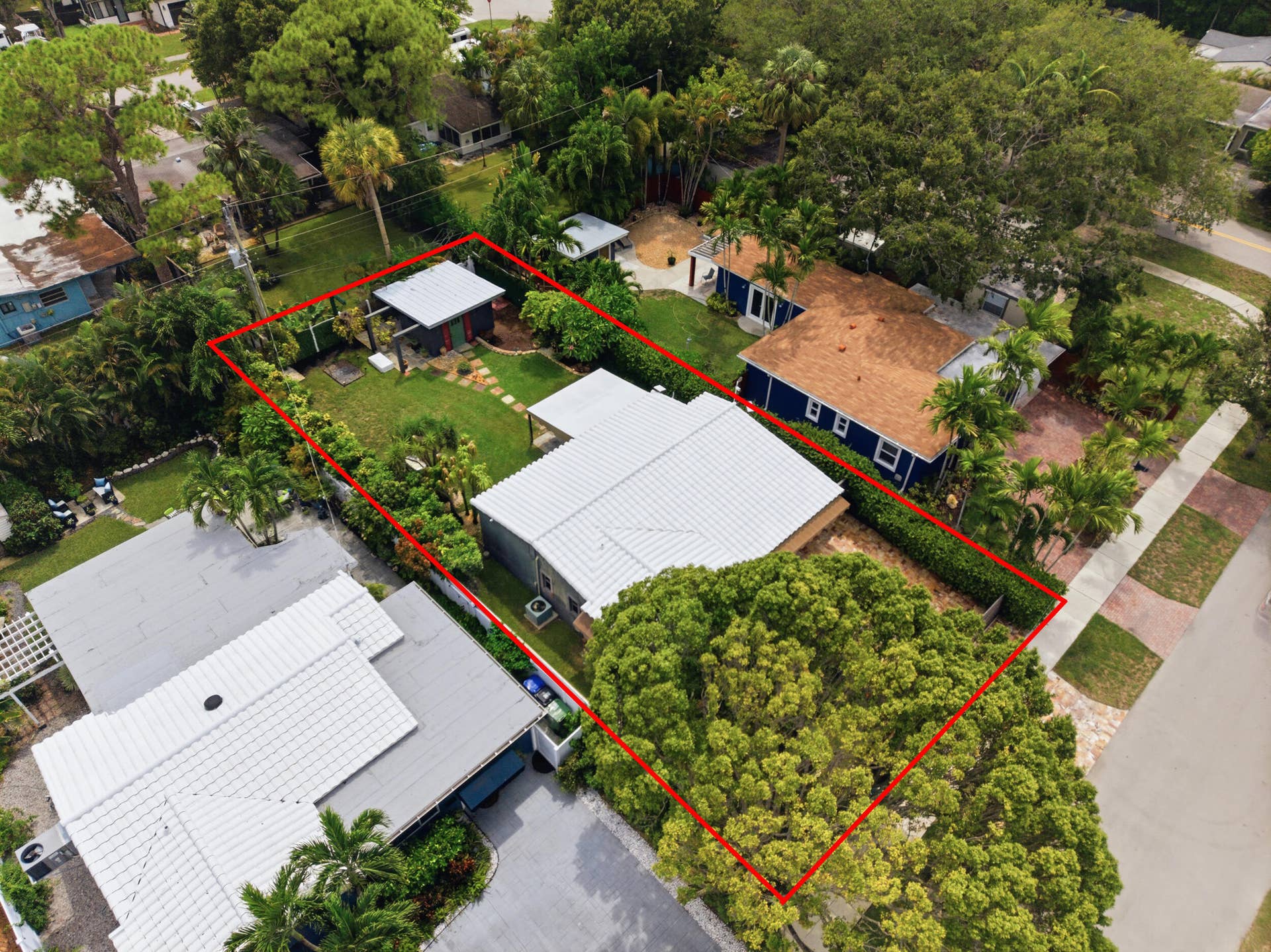 1110 SW 18TH Court, Fort Lauderdale, FL 33315 Aerial perspective of a property featuring a metal roof, stone-paved walkway, detached storage structure, manicured lawn, and mature canopy trees