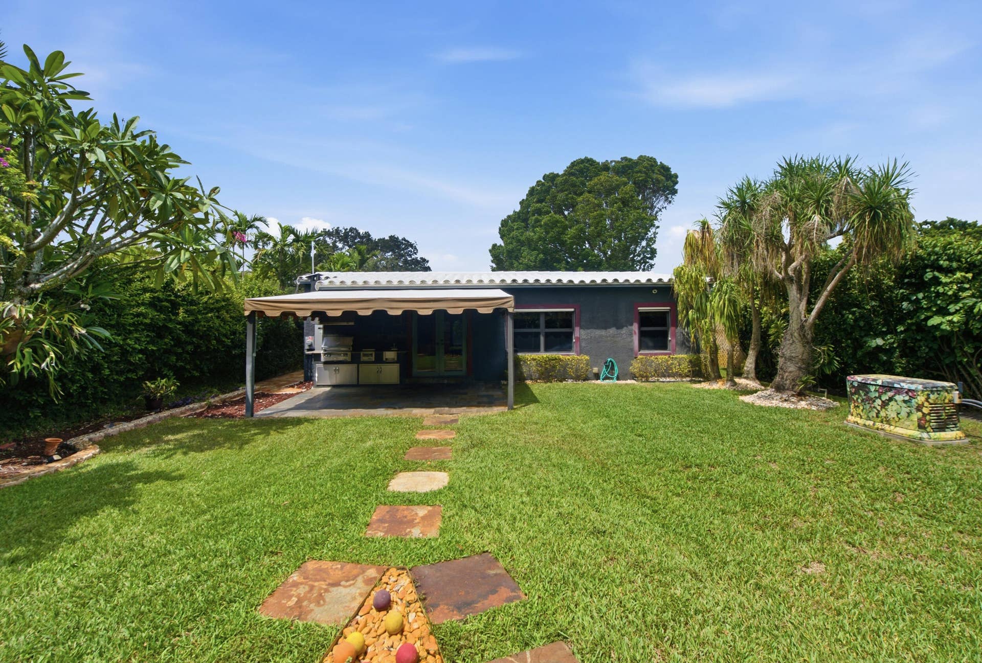 1110 SW 18TH Court, Fort Lauderdale, FL 33315 Backyard featuring a covered patio, stone paver pathway, mature tropical landscaping, and a fenced perimeter