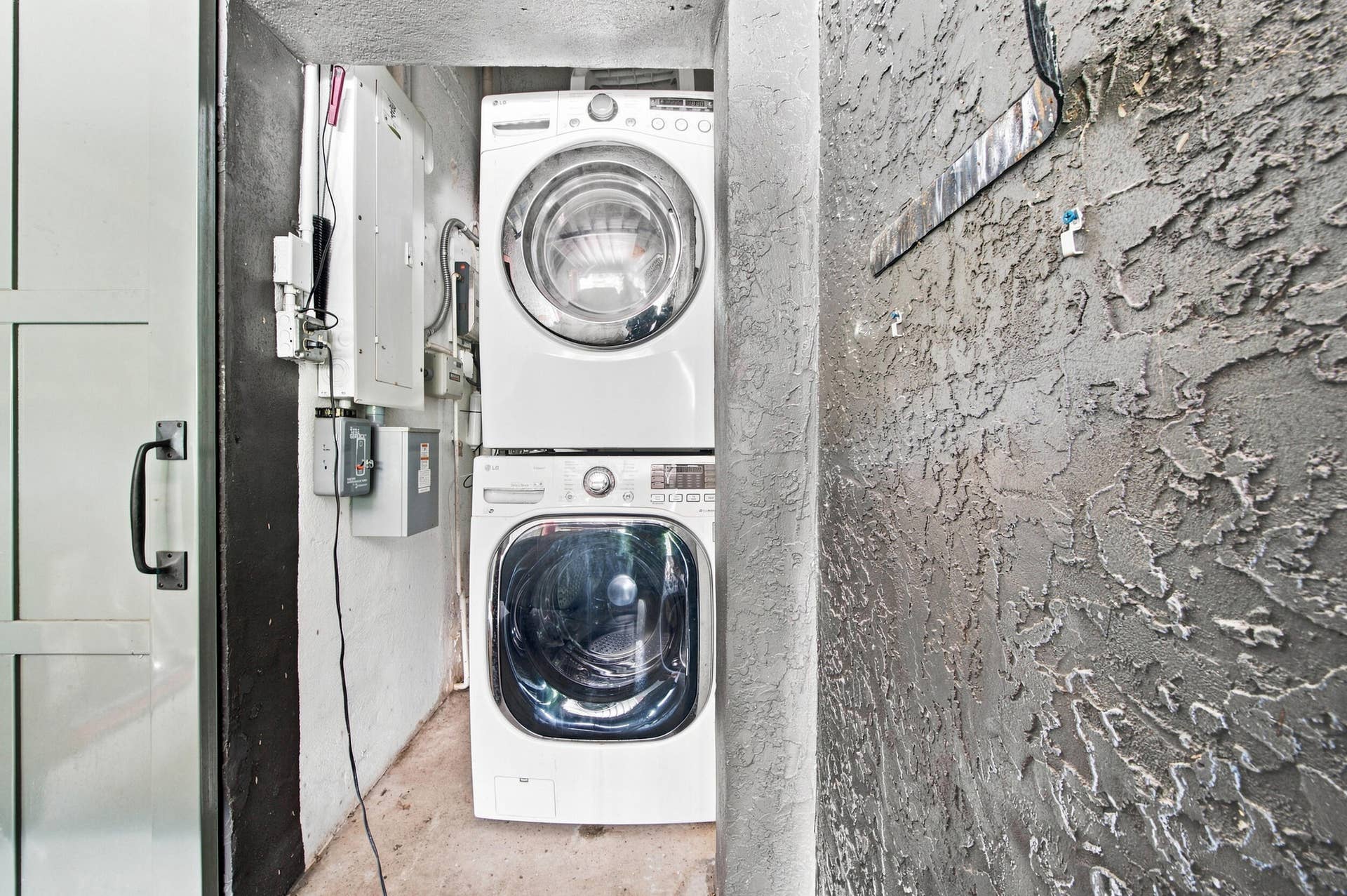 1110 SW 18TH Court, Fort Lauderdale, FL 33315 Laundry alcove featuring a stacked front-loading washer and dryer, textured concrete wall finish, and an integrated electrical panel