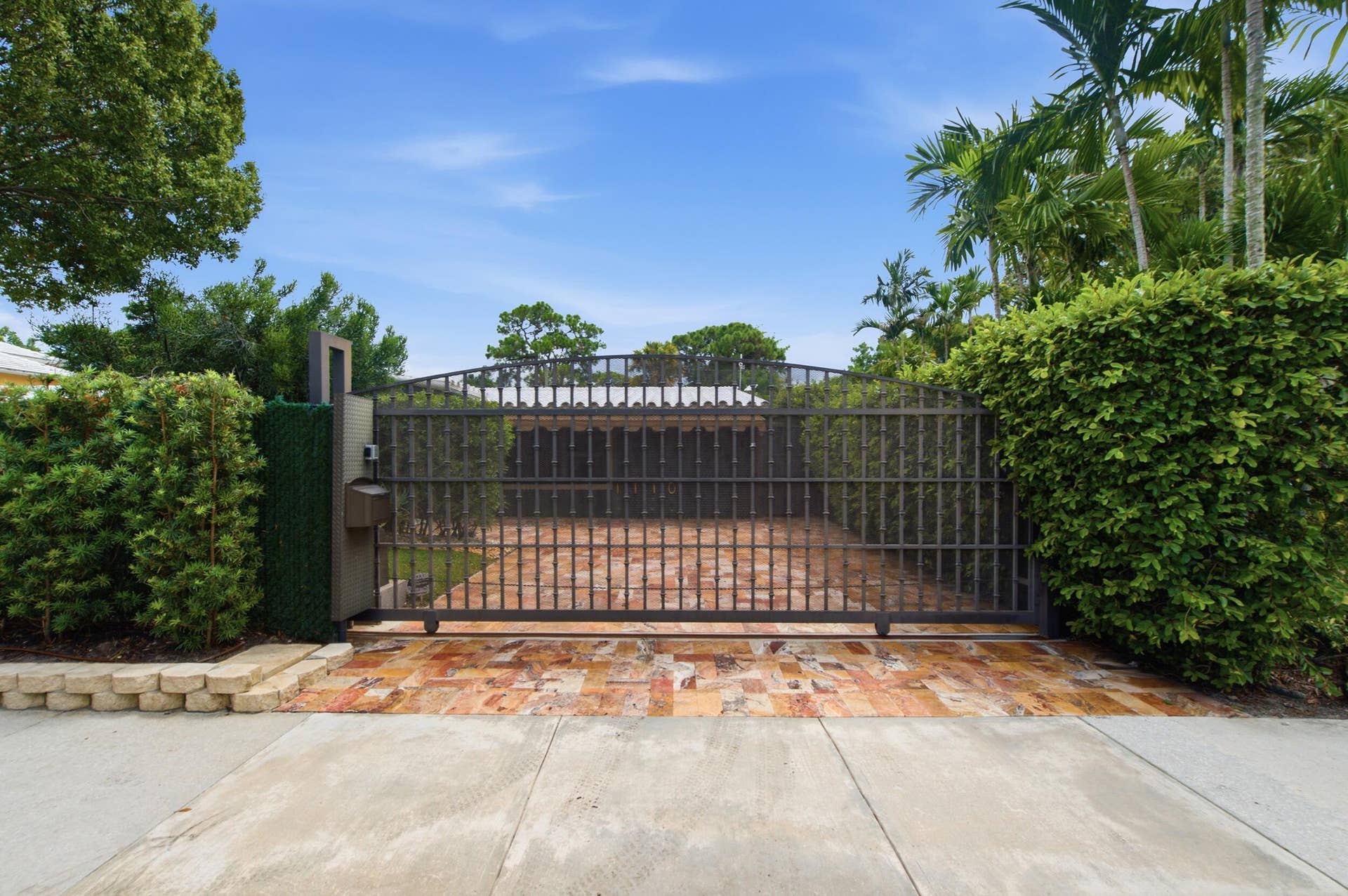 1110 SW 18TH Court, Fort Lauderdale, FL 33315 Private entrance featuring a motorized wrought iron gate, stone-paved driveway, and perimeter hedges