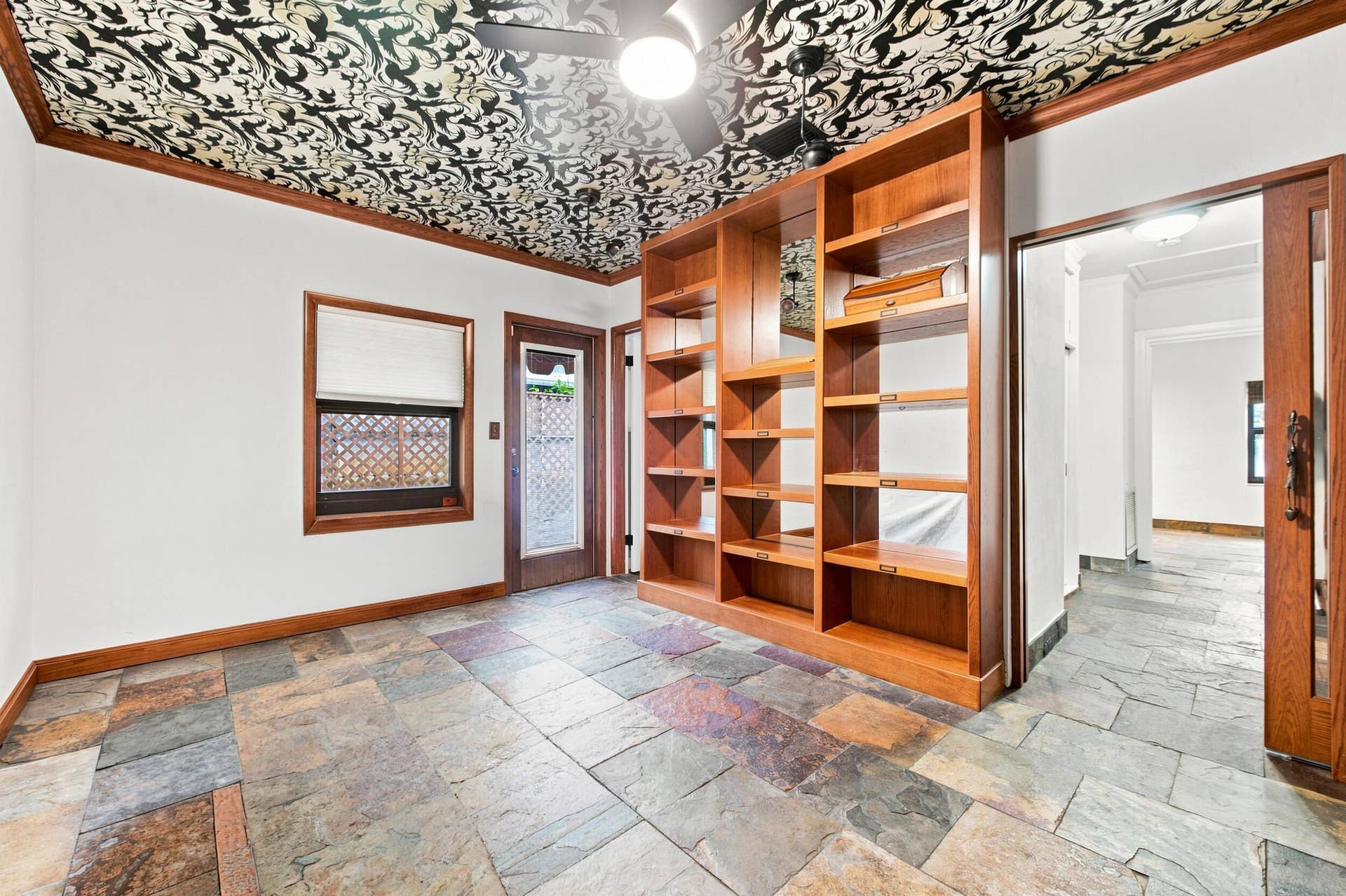 1110 SW 18TH Court, Fort Lauderdale, FL 33315 Room featuring natural stone tile flooring, floor-to-ceiling built-in wood shelving, intricate patterned ceiling treatment, and wood-trimmed window and door frames