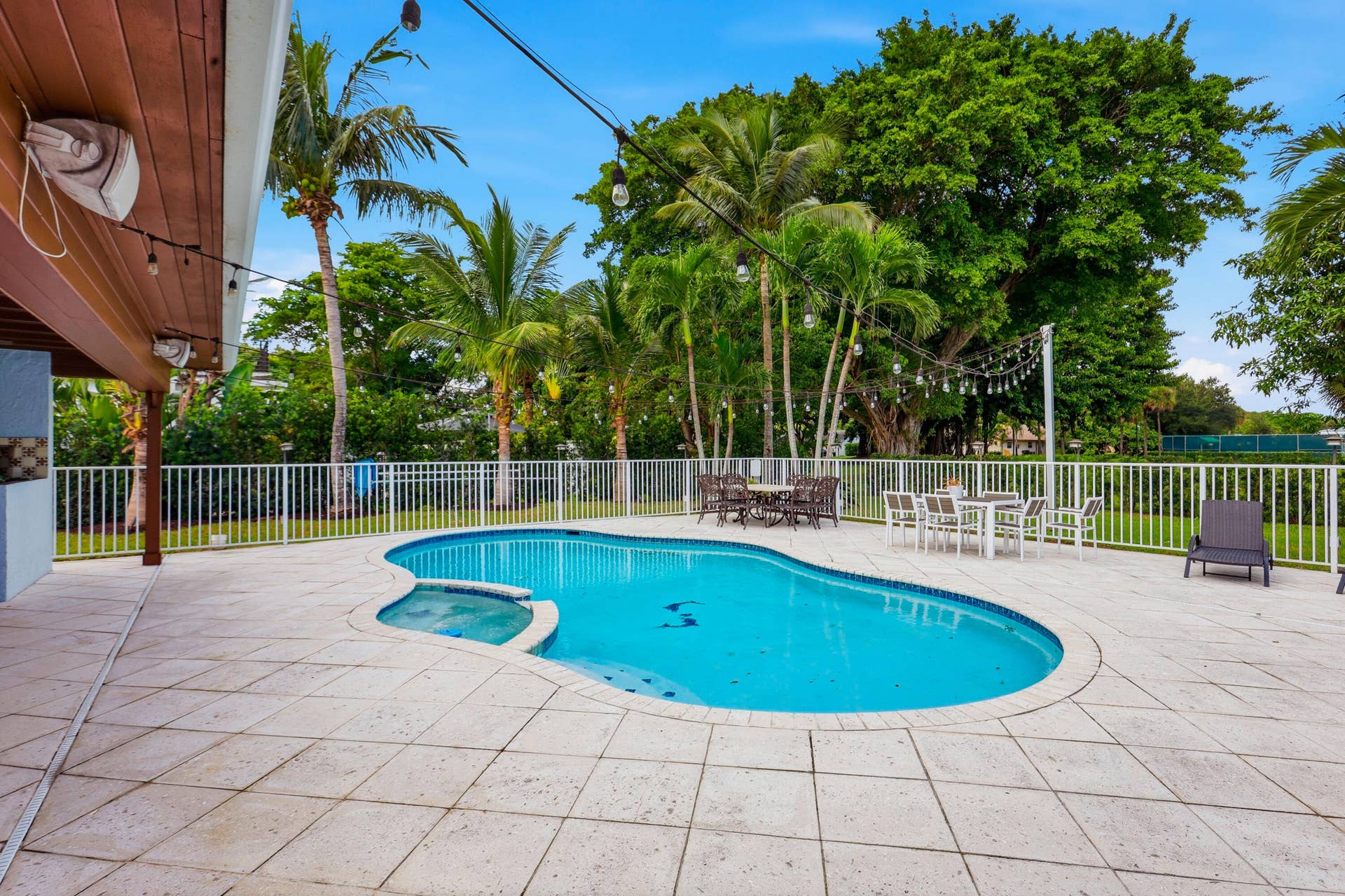 2919 Banyan Blvd Circle NW, Boca Raton, FL 33431 Outdoor living area featuring a custom-shaped swimming pool with integrated spa, expansive stone paver patio, covered porch with wood-finish ceiling, and perimeter metal fencing