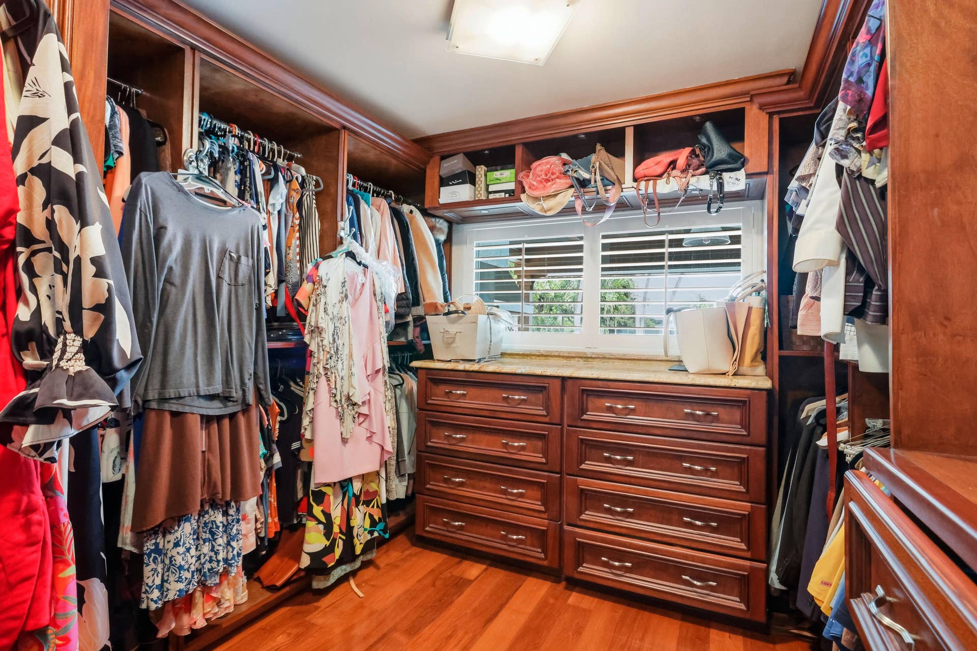 2919 Banyan Blvd Circle NW, Boca Raton, FL 33431 Custom walk-in closet featuring extensive dark wood cabinetry, integrated drawer storage, overhead shelving, plantation shutters, and polished wood-finish flooring