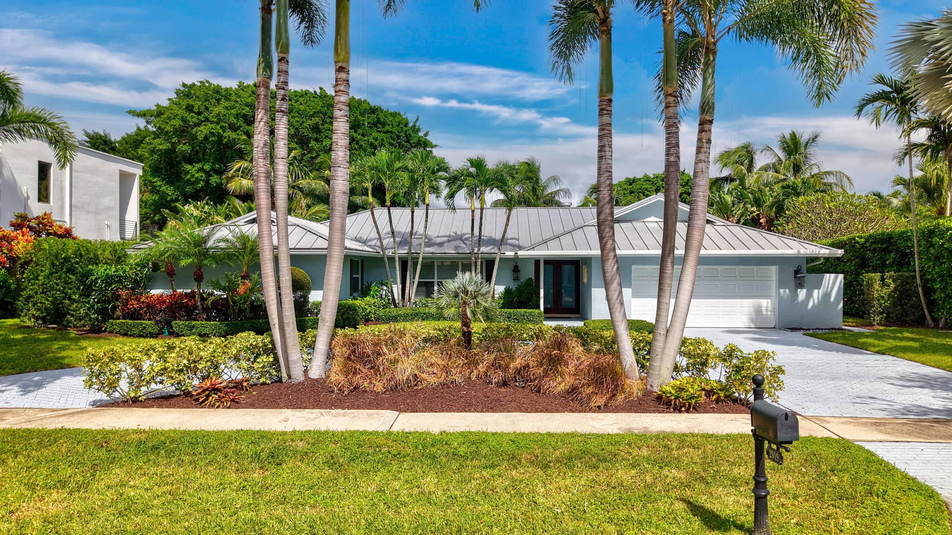 2919 Banyan Blvd Circle NW, Boca Raton, FL 33431 Single-story residence featuring a standing-seam metal roof, attached garage, stone-paved driveway, and mature palm trees