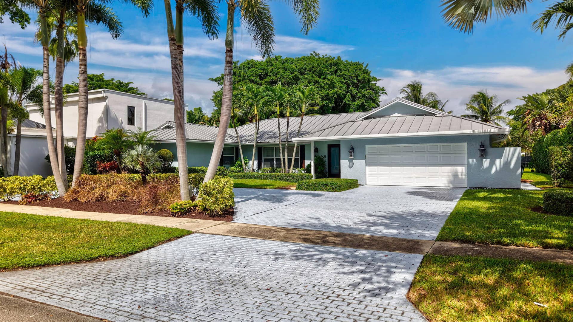 2919 Banyan Blvd Circle NW, Boca Raton, FL 33431 Single-story residence featuring a standing seam metal roof, paved driveway, two-car garage, and established tropical landscaping