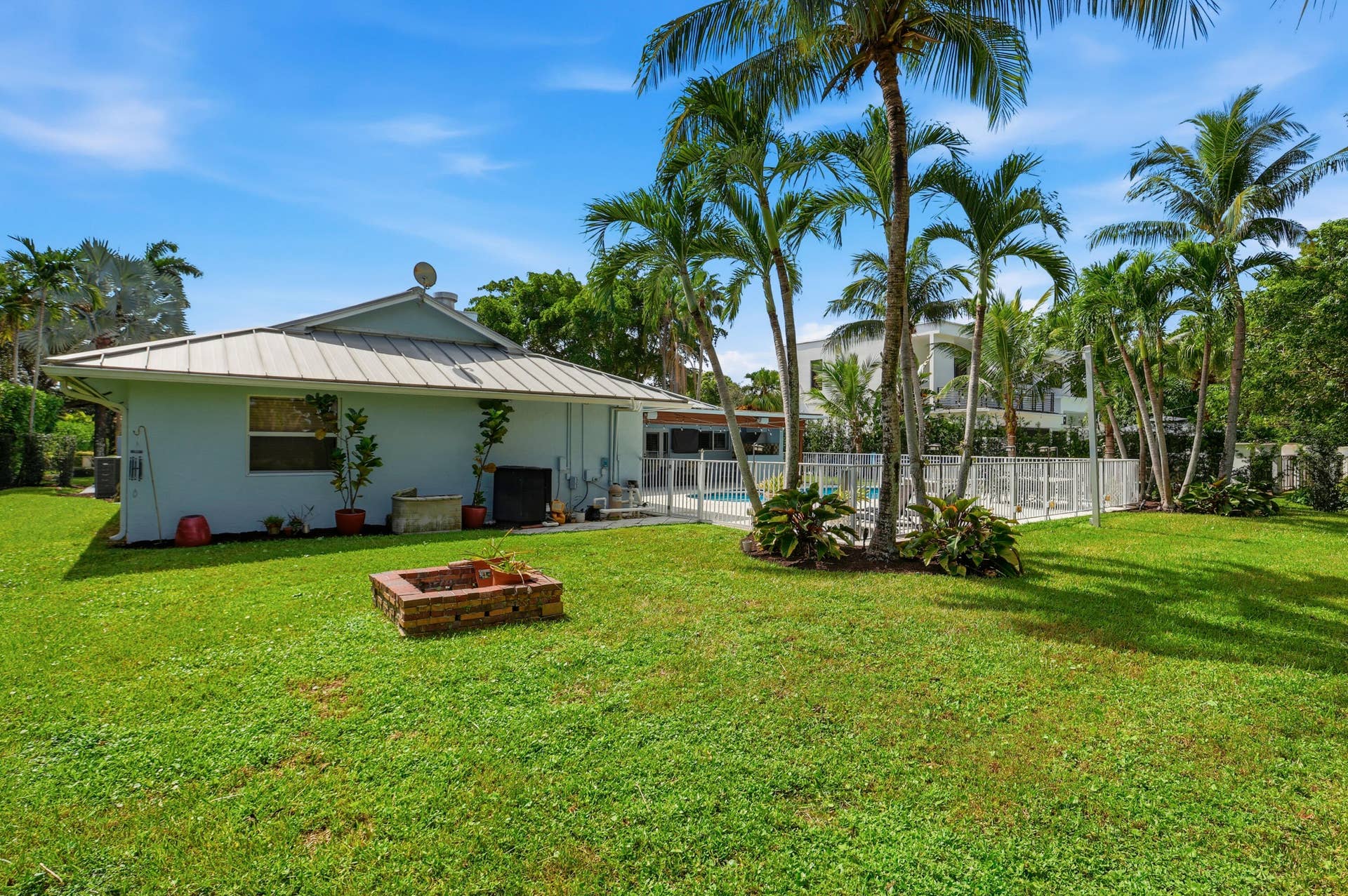 2919 Banyan Blvd Circle NW, Boca Raton, FL 33431 Expansive backyard featuring a metal roof structure, a masonry fire pit, mature palm trees, and a fenced swimming pool area