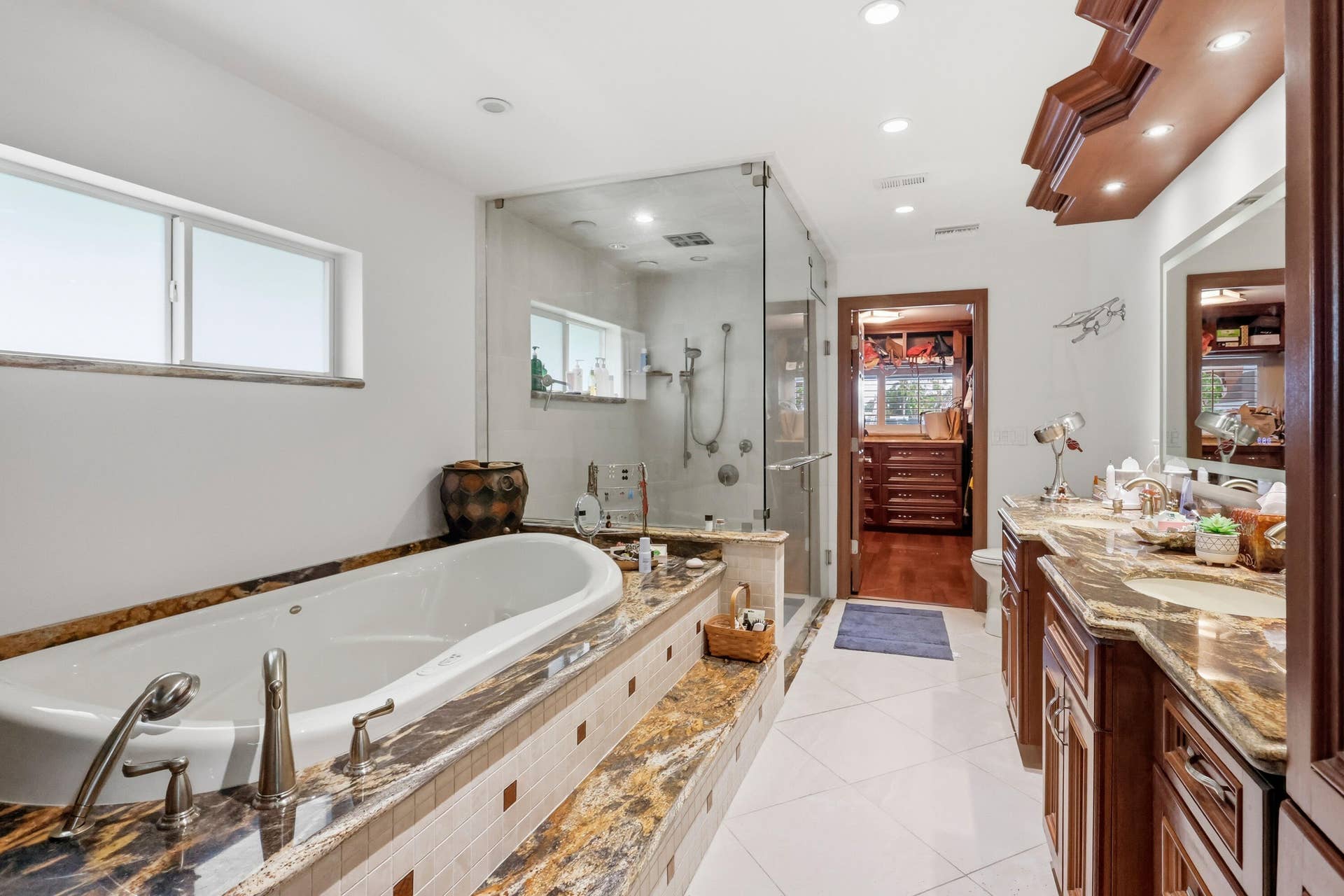 2919 Banyan Blvd Circle NW, Boca Raton, FL 33431 Bathroom featuring a jetted soaking tub with stone surround, custom wood-finish cabinetry, stone countertop, glass-enclosed shower, and tile flooring