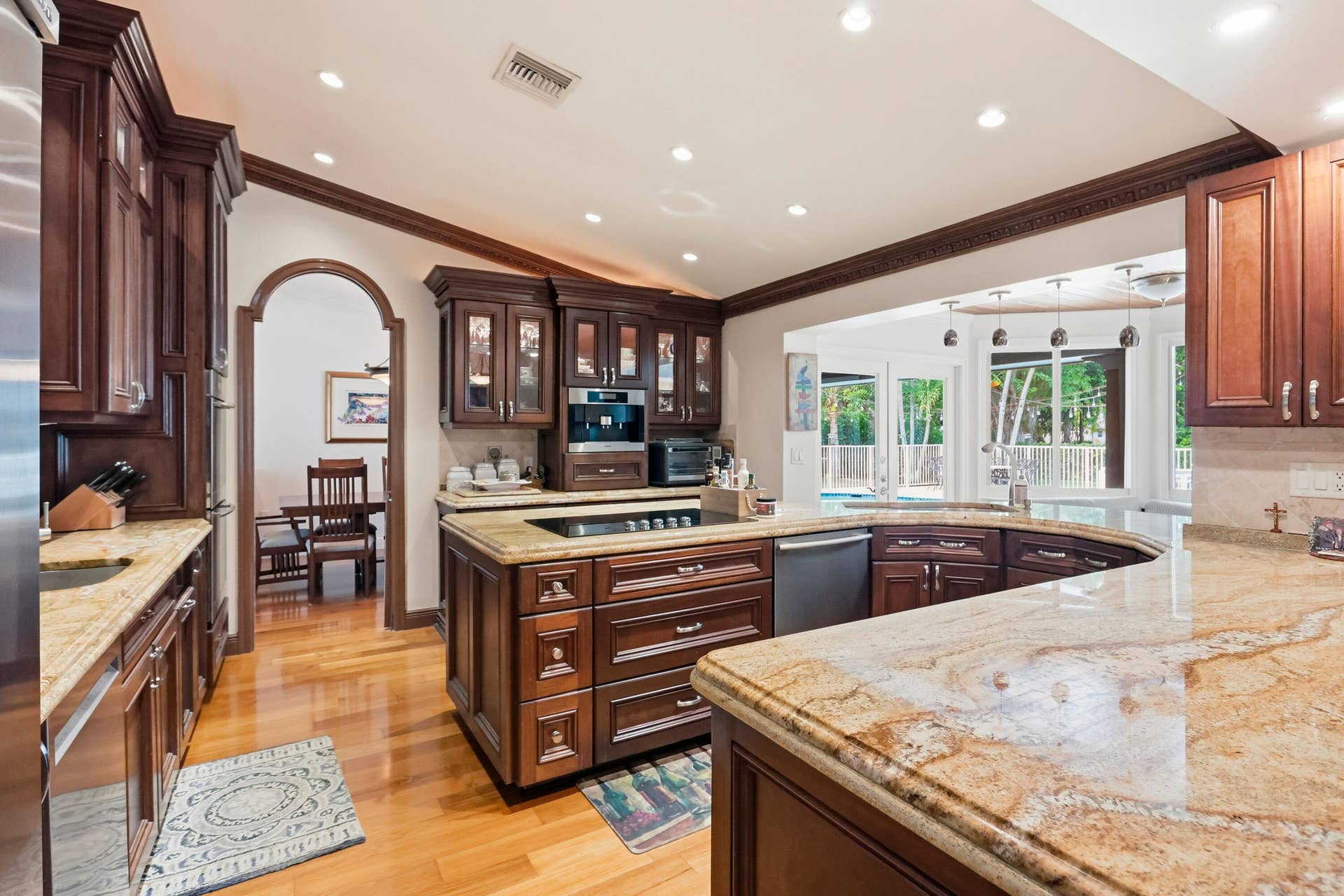 2919 Banyan Blvd Circle NW, Boca Raton, FL 33431 Kitchen featuring wood cabinetry, stone countertops, integrated cooktop, recessed lighting, and arched doorway