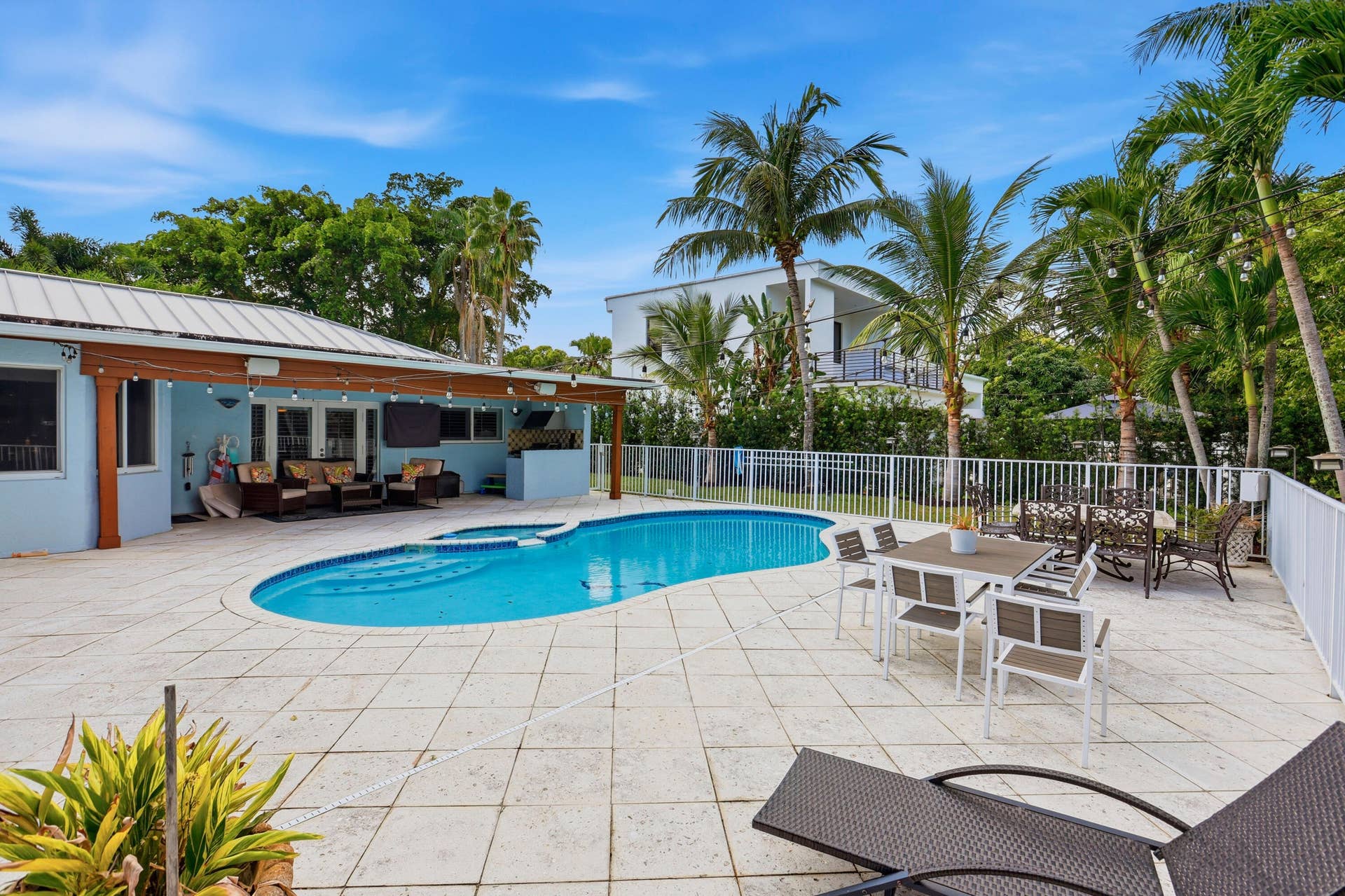 2919 Banyan Blvd Circle NW, Boca Raton, FL 33431 Outdoor swimming pool featuring a spillover spa, expansive paved patio, wood-post covered lanai, and white metal perimeter fencing