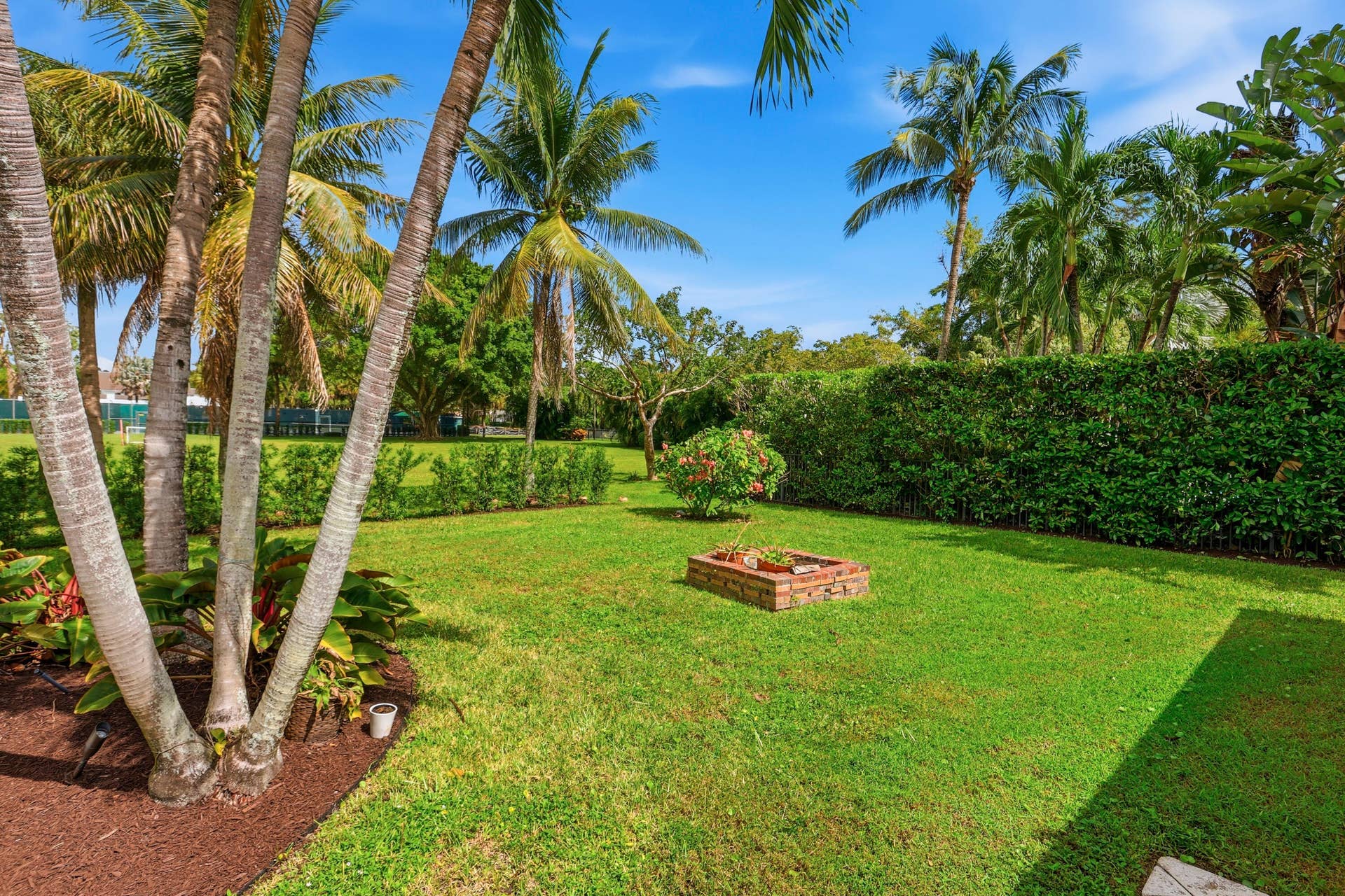 2919 Banyan Blvd Circle NW, Boca Raton, FL 33431 Backyard featuring a manicured lawn, perimeter privacy hedge, mature palm trees, and a brick-bordered garden bed