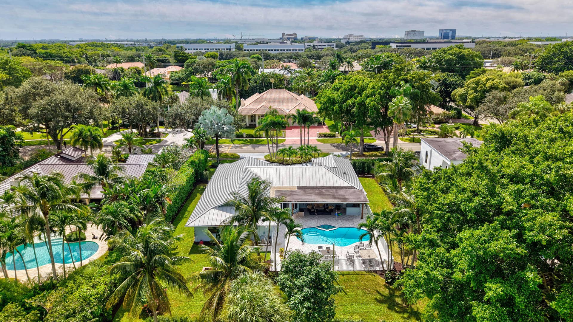 2919 Banyan Blvd Circle NW, Boca Raton, FL 33431 Aerial perspective featuring a single-story residence with a metal roof, an in-ground swimming pool, a stone-paved patio, and mature tropical landscaping