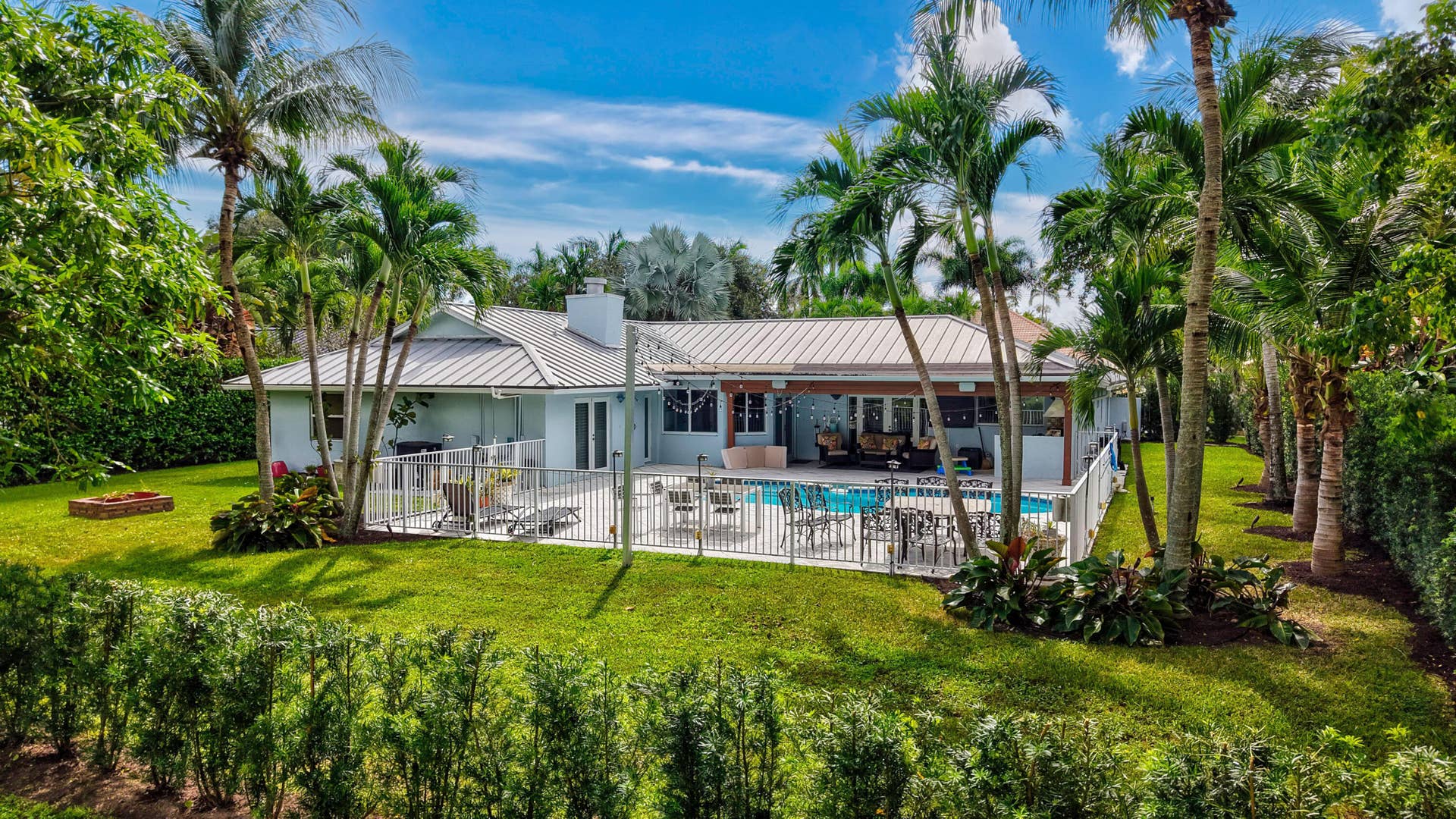 2919 Banyan Blvd Circle NW, Boca Raton, FL 33431 Backyard featuring a swimming pool, covered patio, metal roof, and manicured landscaping with mature palm trees