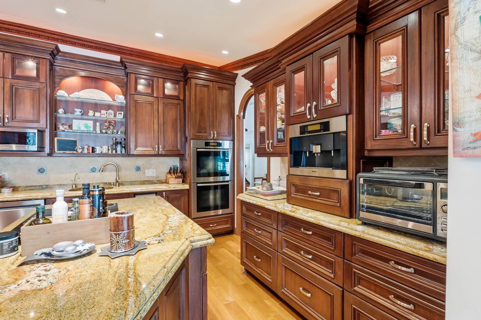 2919 Banyan Blvd Circle NW, Boca Raton, FL 33431 Custom dark-wood cabinetry with glass-panel upper doors, stone countertops, double wall ovens, integrated built-in coffee station, and wood-finish flooring
