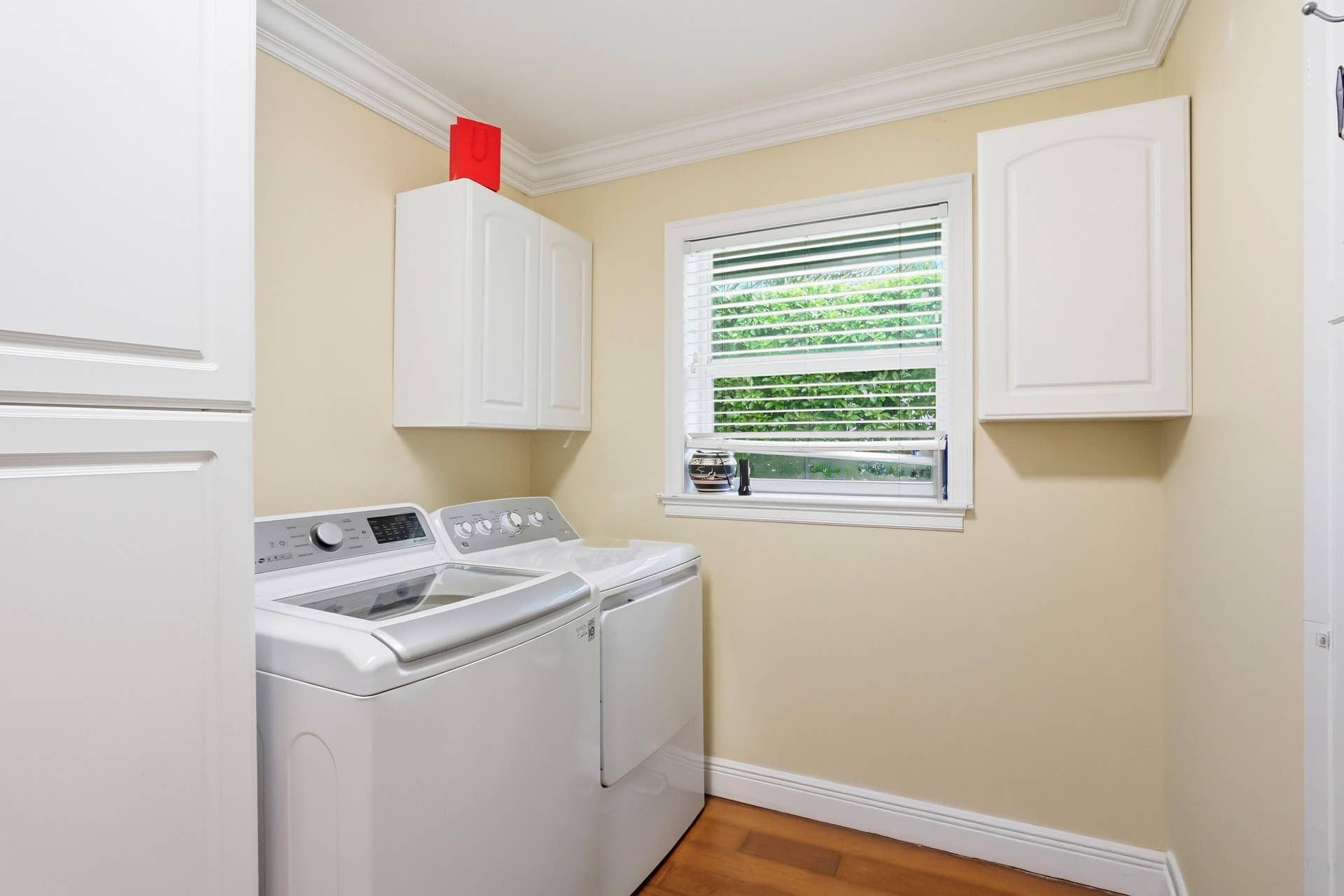 2919 Banyan Blvd Circle NW, Boca Raton, FL 33431 Laundry room featuring white wall-mounted cabinetry, wood-finish flooring, crown molding, and a single-hung window