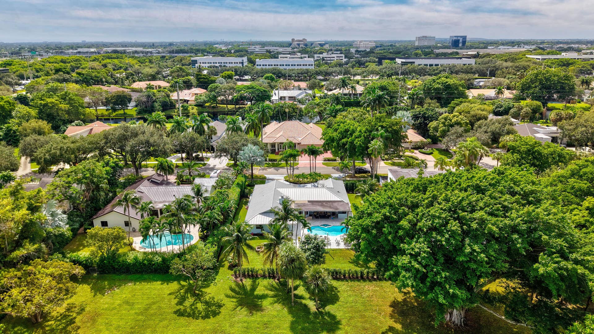 2919 Banyan Blvd Circle NW, Boca Raton, FL 33431 Aerial perspective featuring expansive landscaped grounds, mature canopy trees, multiple in-ground swimming pools, and residential structures with pitched roofing