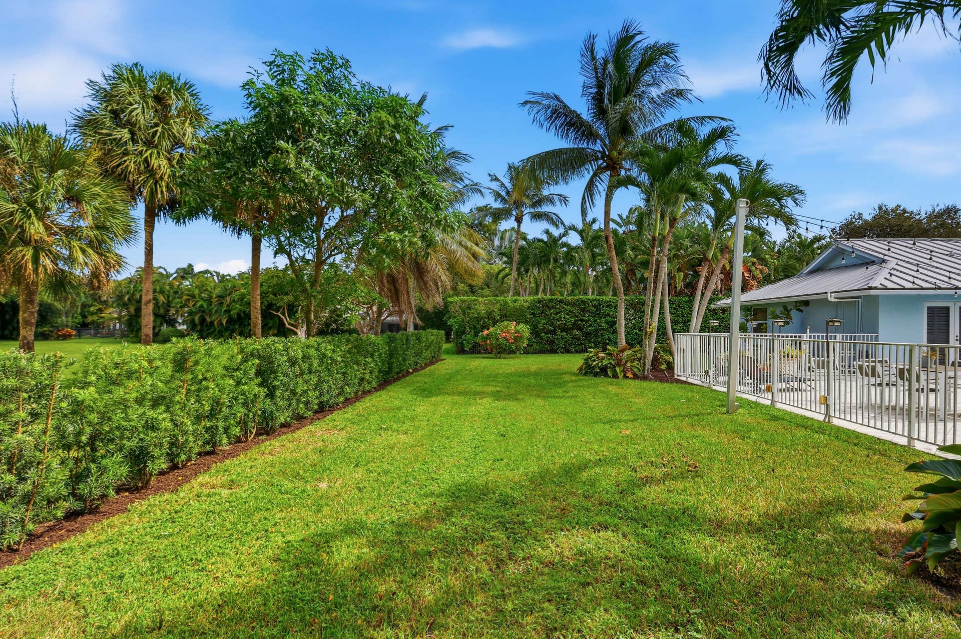 2919 Banyan Blvd Circle NW, Boca Raton, FL 33431 Spacious lawn featuring mature palm trees, manicured hedges, and a fenced pool area with a metal roof structure