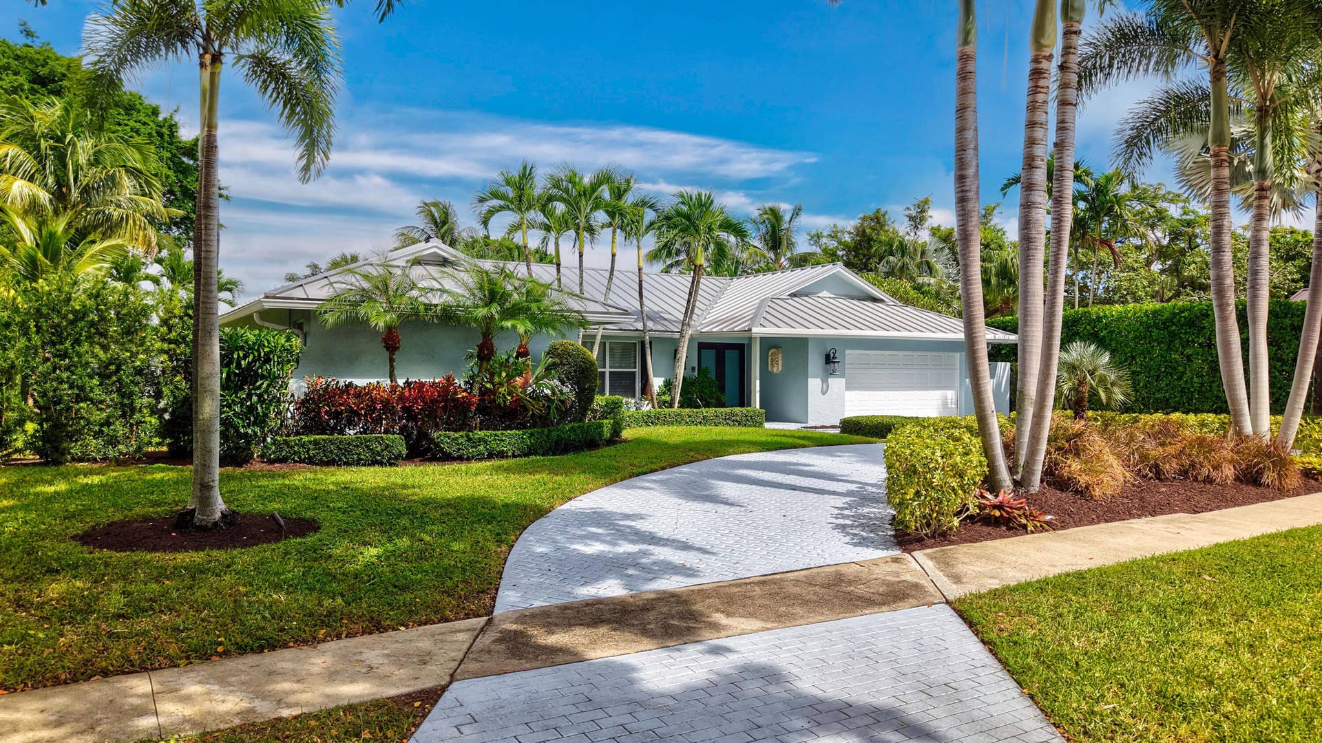 2919 Banyan Blvd Circle NW, Boca Raton, FL 33431 Single-story residence featuring a metal roof, paved driveway, two-car garage, and established landscaping with mature palms