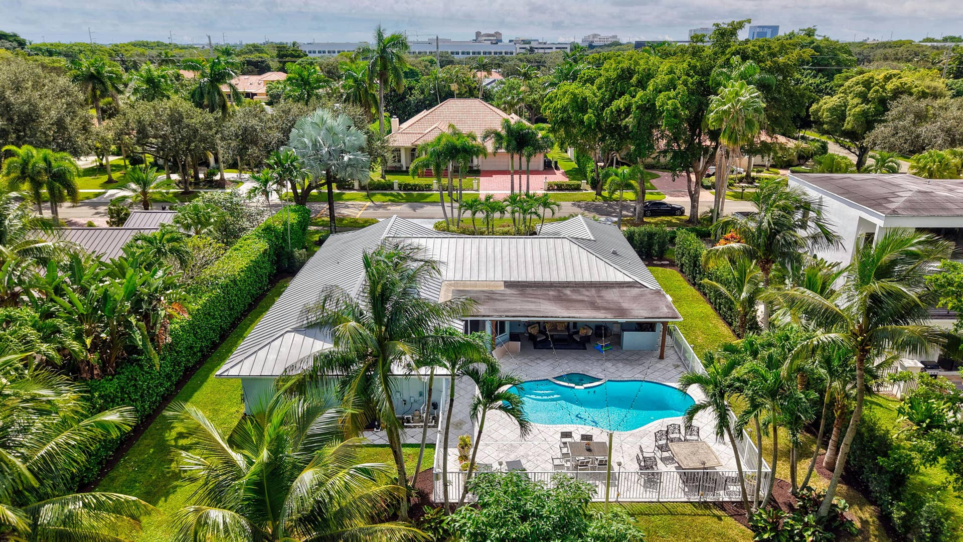 2919 Banyan Blvd Circle NW, Boca Raton, FL 33431 Metal roof residence featuring a swimming pool, covered patio, surrounding privacy hedges, and paved pool deck