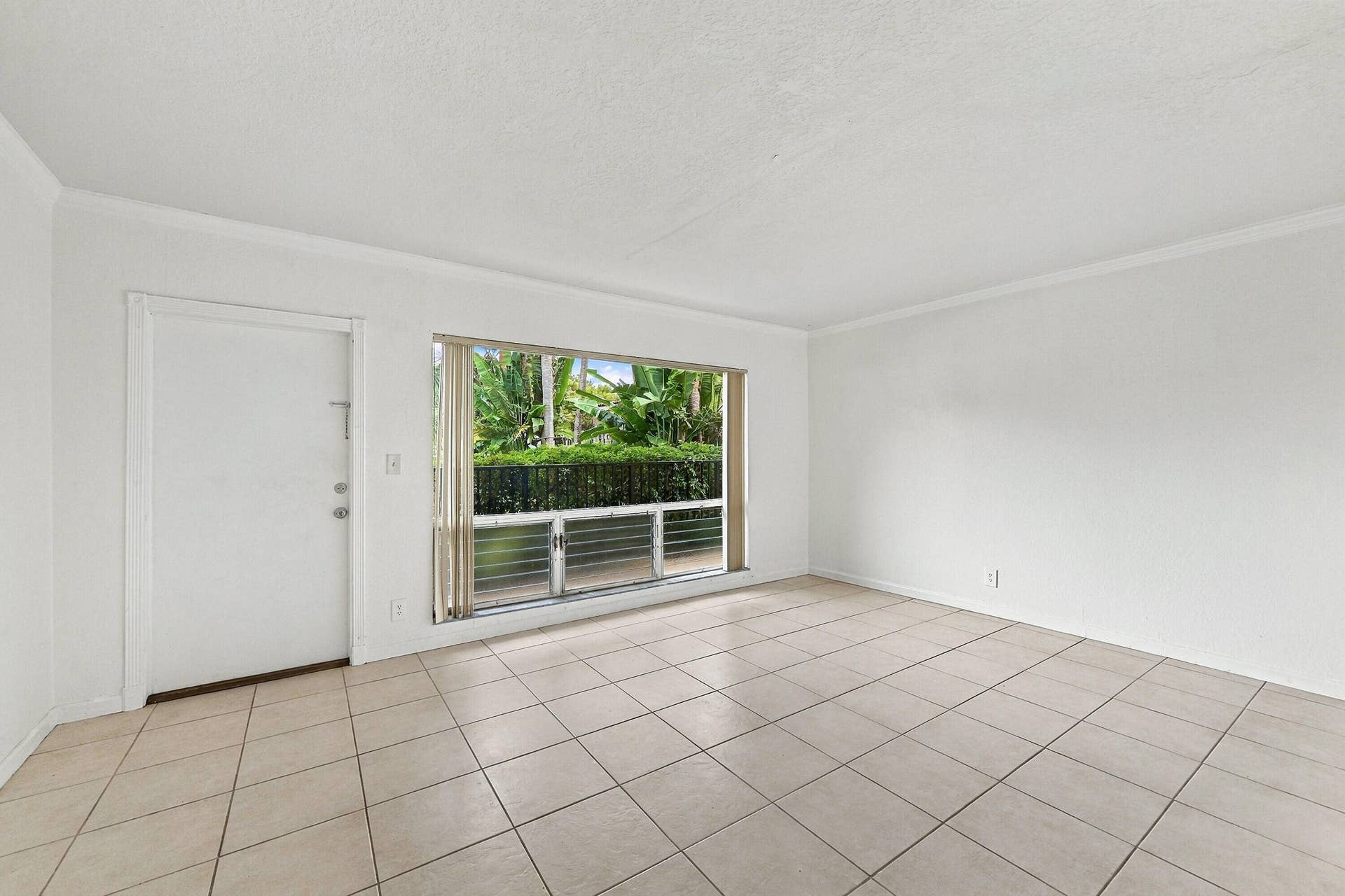 Neutral-toned ceramic tile flooring, large picture window with horizontal mullions, solid-core entry door, and crisp white wall finishes