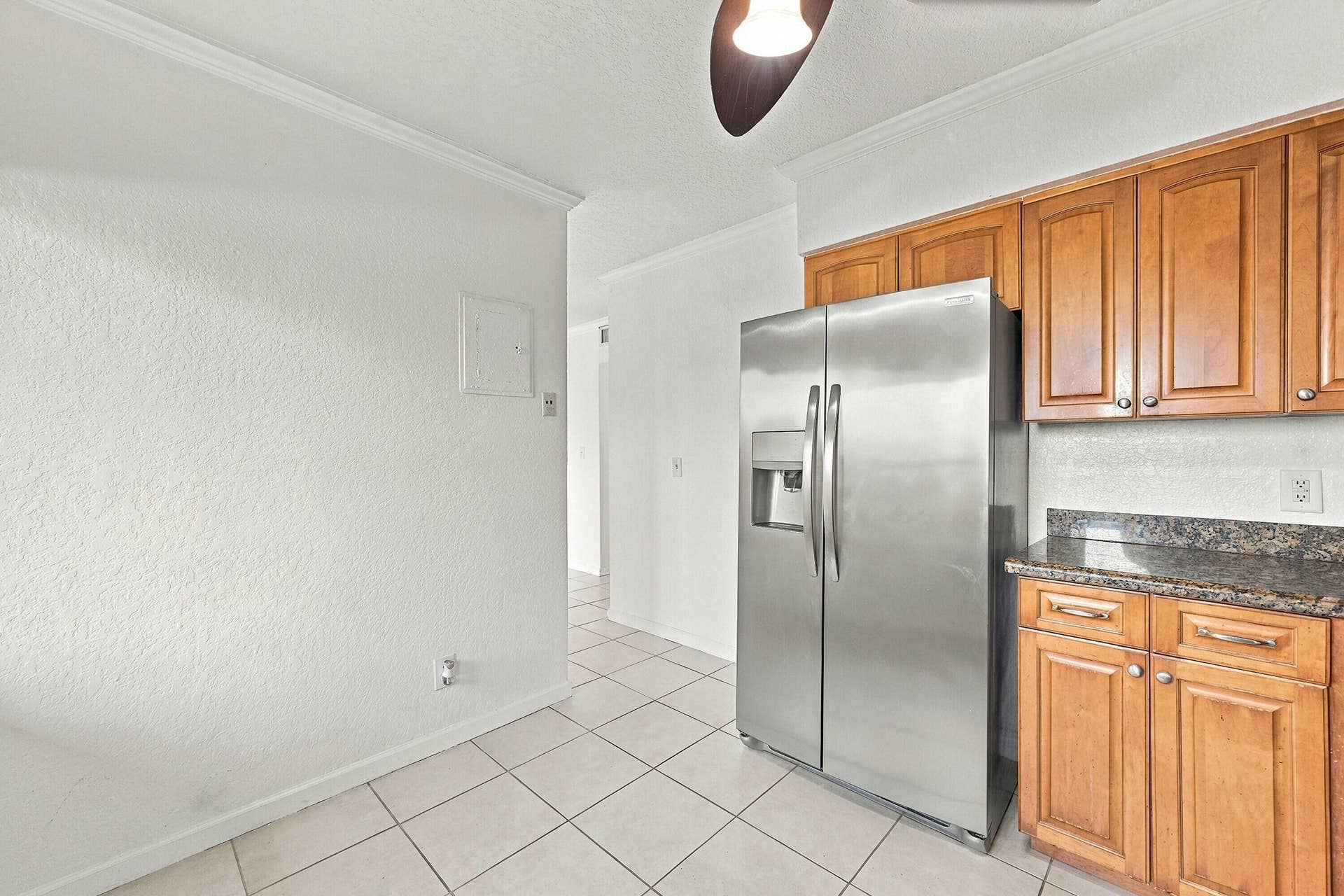 Kitchen area featuring wood cabinetry, stone-finish countertops, stainless steel side-by-side refrigerator, and tile flooring
