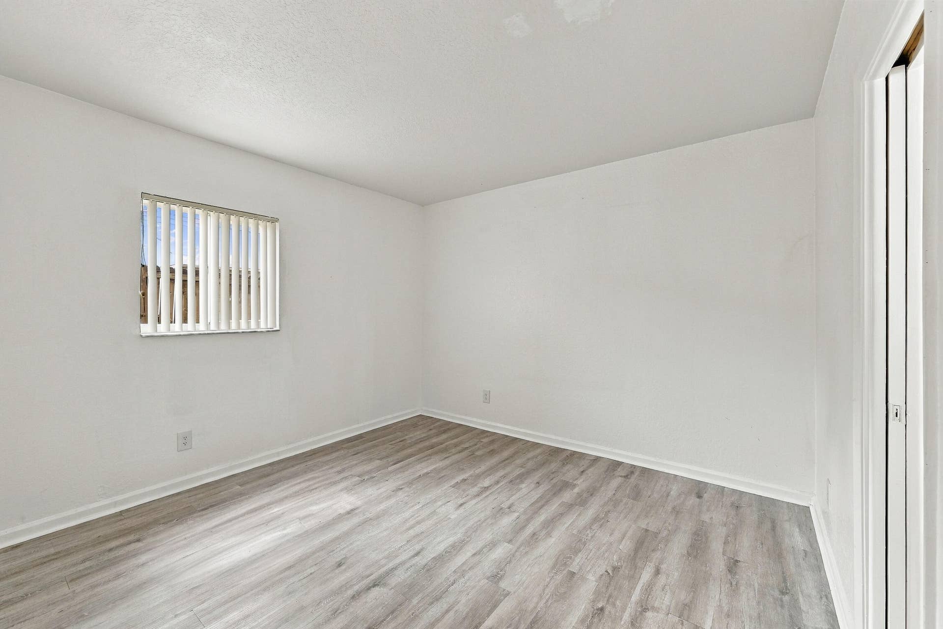 Neutral interior featuring wood-finish flooring, white walls, and a single-pane window with vertical blinds