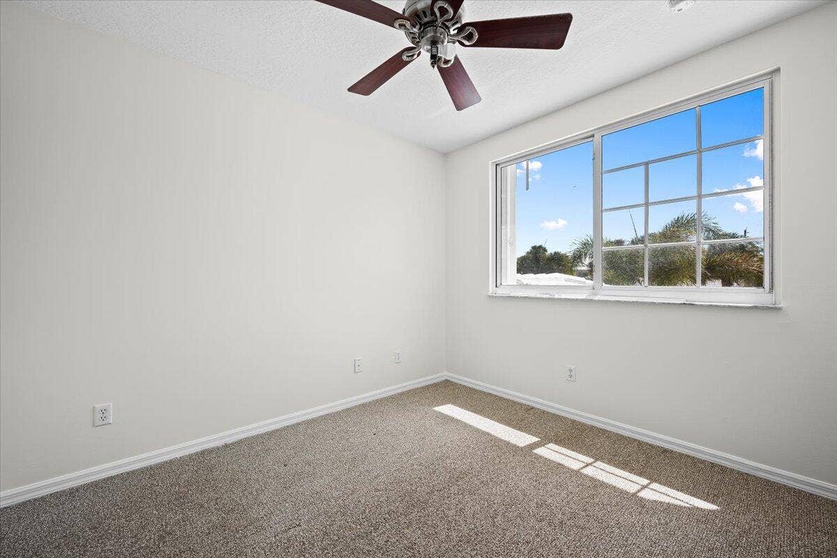 Bright bedroom with carpeting, ceiling fan, and a large window providing natural light.