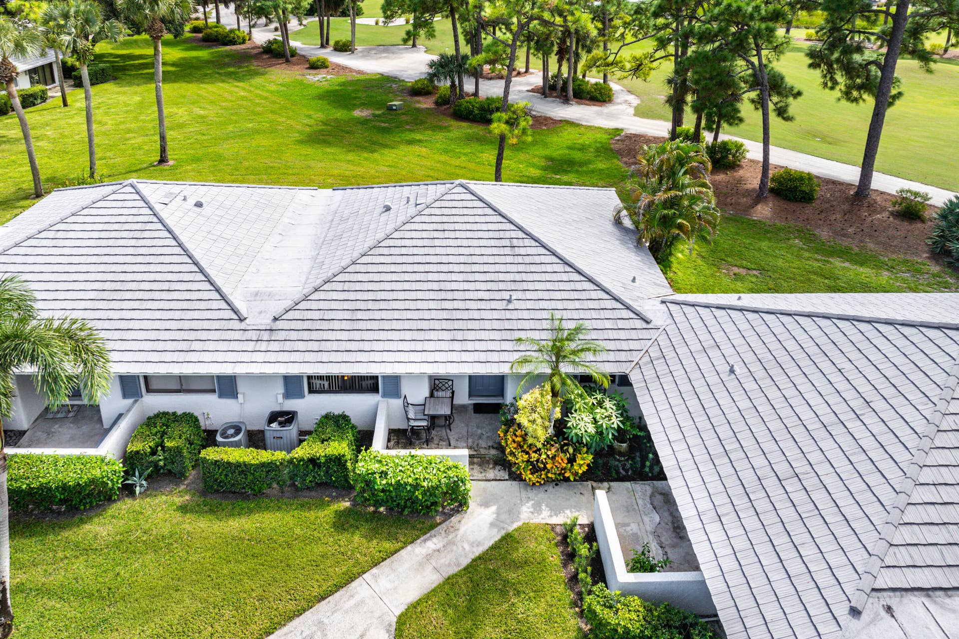 526 Club Drive, Palm Beach Gardens, FL 33418 Exterior perspective featuring a multi-gabled tile roof, manicured lawn, established landscaping, and paved outdoor patio area