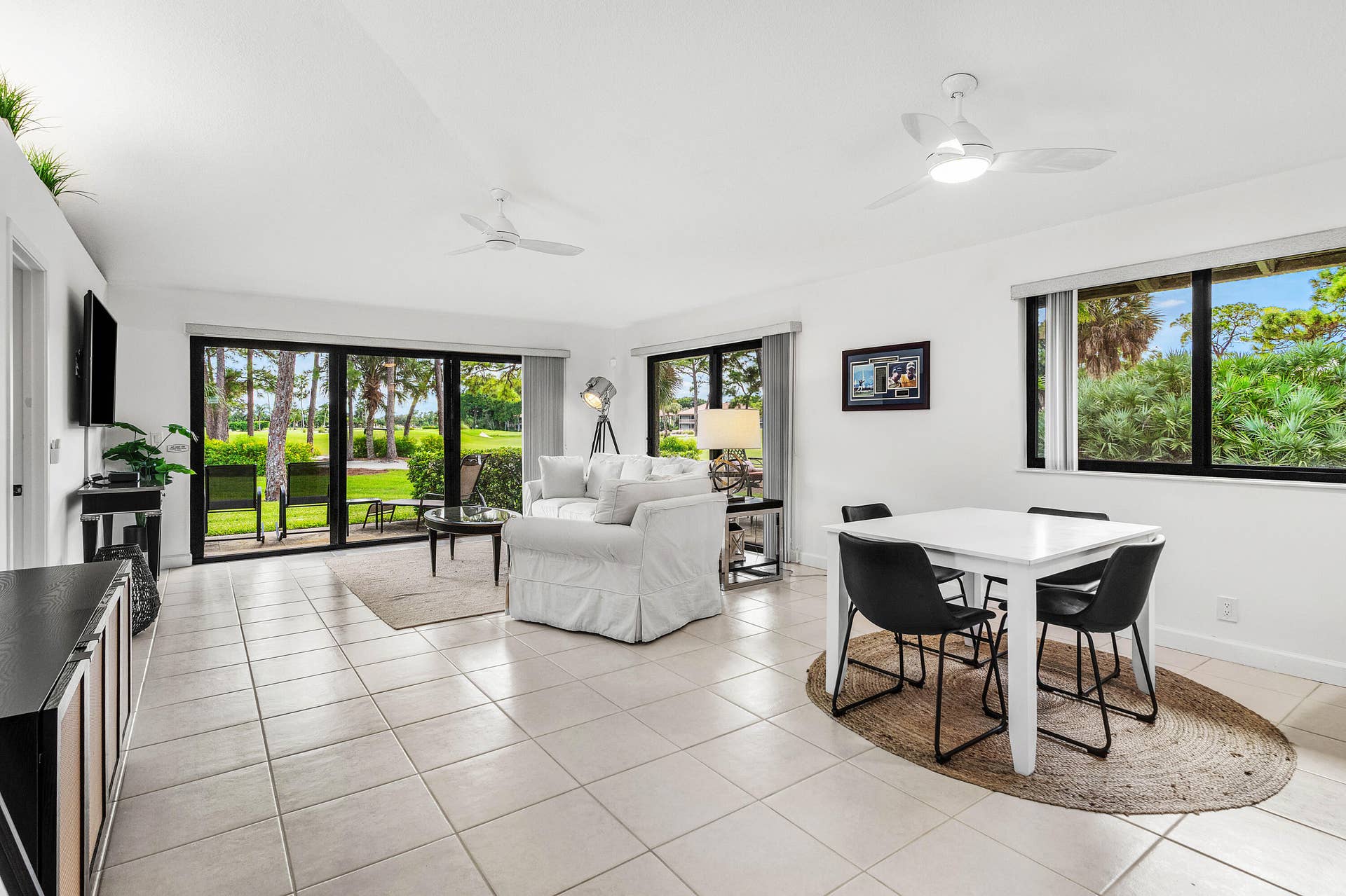 526 Club Drive, Palm Beach Gardens, FL 33418 Open-concept interior featuring large-format ceramic tile flooring, expansive sliding glass doors, black-framed windows, and dual ceiling fans