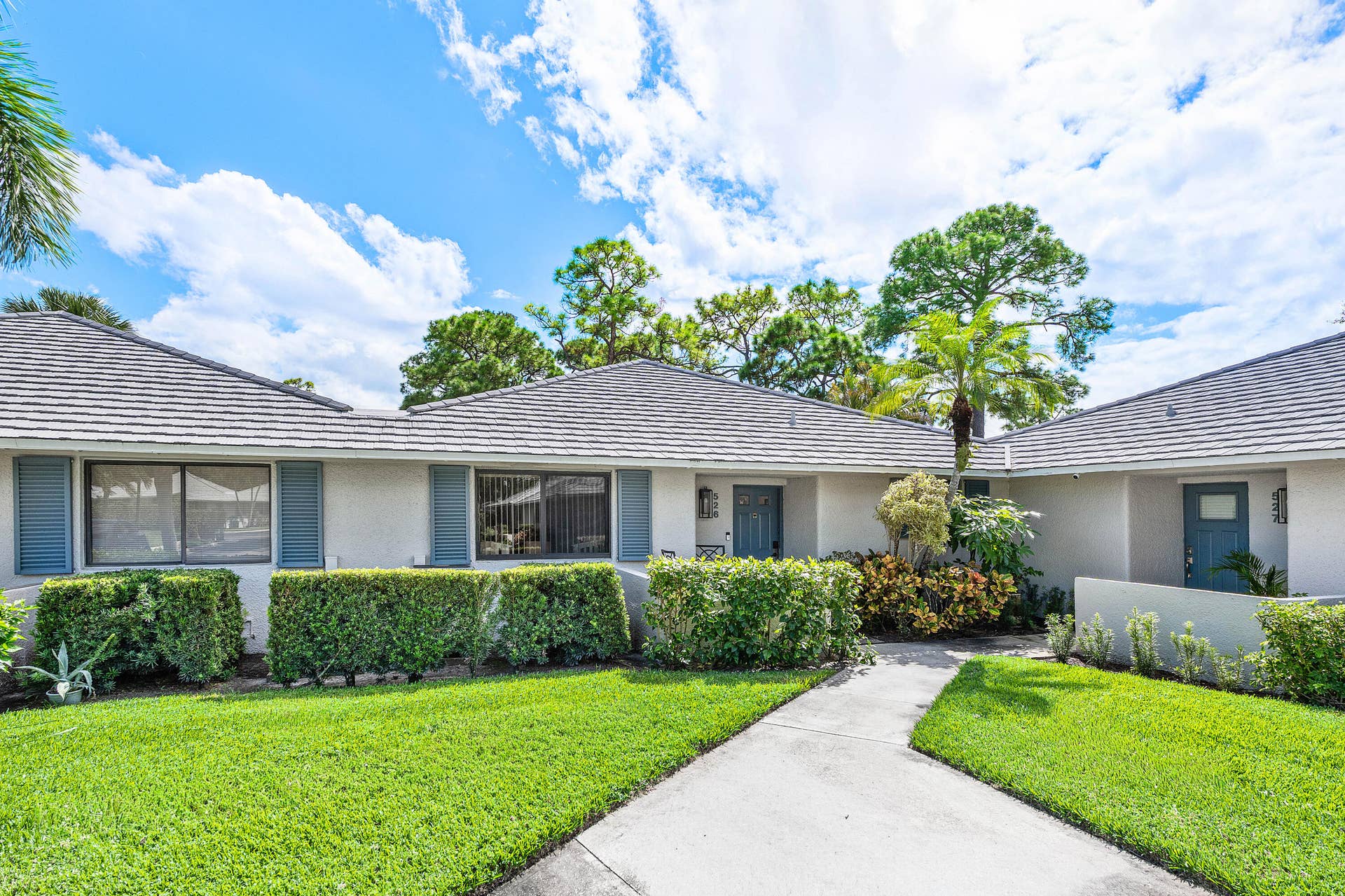 526 Club Drive, Palm Beach Gardens, FL 33418 Single-story exterior featuring a concrete tile roof, neutral stucco finish, decorative shutters, and manicured landscaping