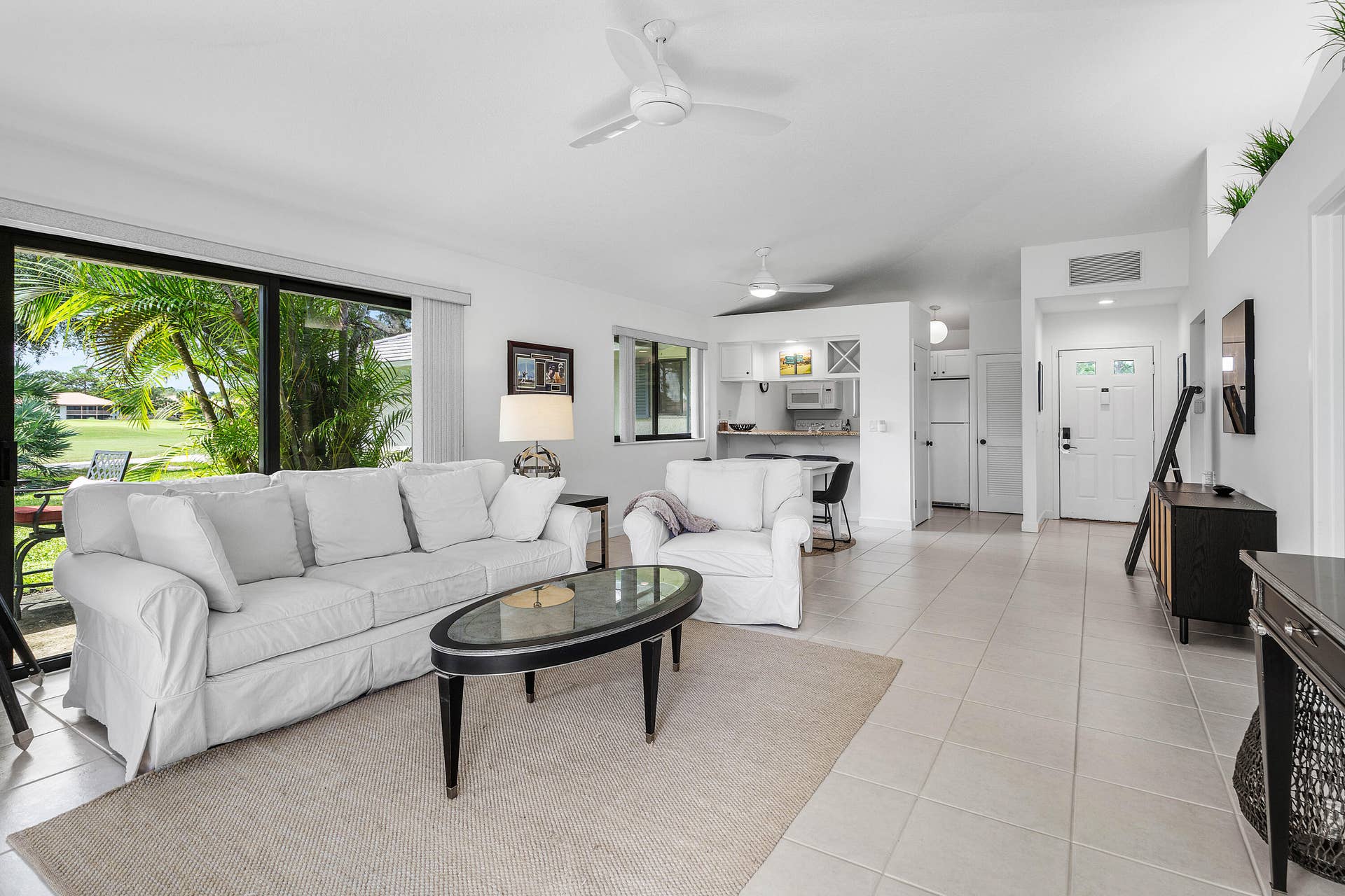 526 Club Drive, Palm Beach Gardens, FL 33418 Open-concept living space featuring ceramic tile flooring, floor-to-ceiling sliding glass doors, built-in kitchen cabinetry, and overhead ceiling fans