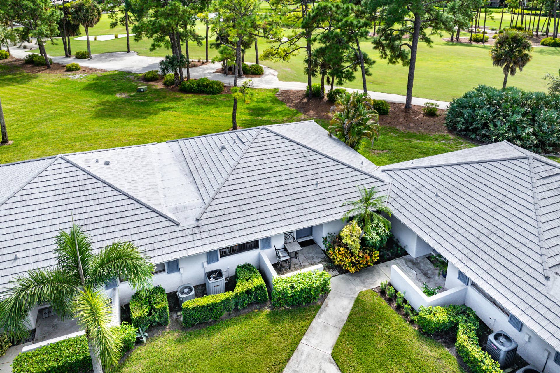526 Club Drive, Palm Beach Gardens, FL 33418 Multi-pitched concrete tile roof, manicured lawn, established landscaping, and paved walkway set against a backdrop of mature trees and open green space