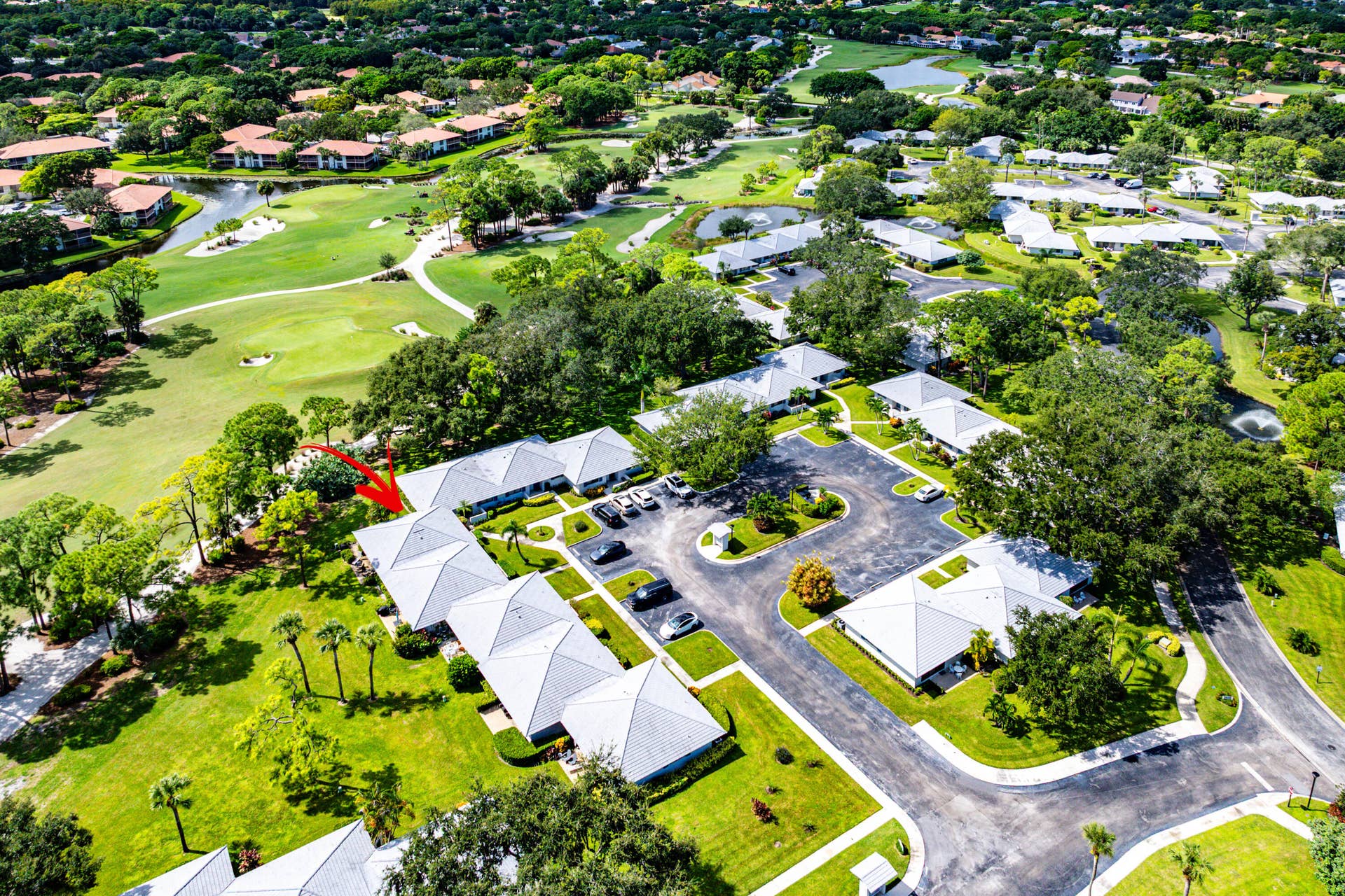 526 Club Drive, Palm Beach Gardens, FL 33418 Aerial perspective featuring a single-story structure with a multi-gabled roof, positioned on a manicured lawn with mature trees and paved surface parking